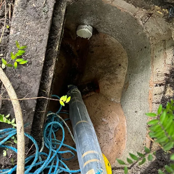 High-pressure water jetting hose clearing a blocked drain in an open outdoor manhole.