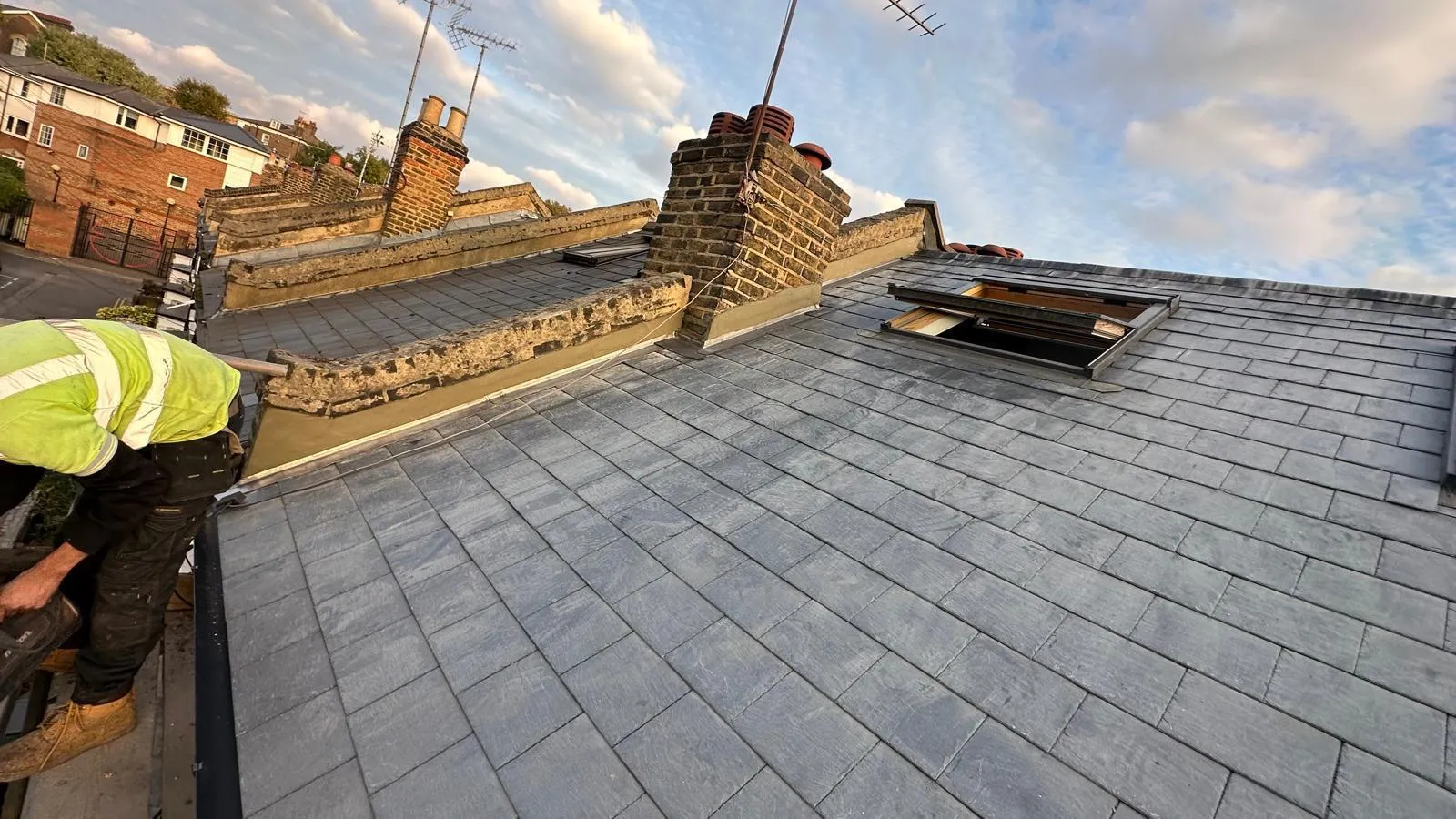 Roofer carrying out slate roof repairs and lead flashing installation on a terraced property