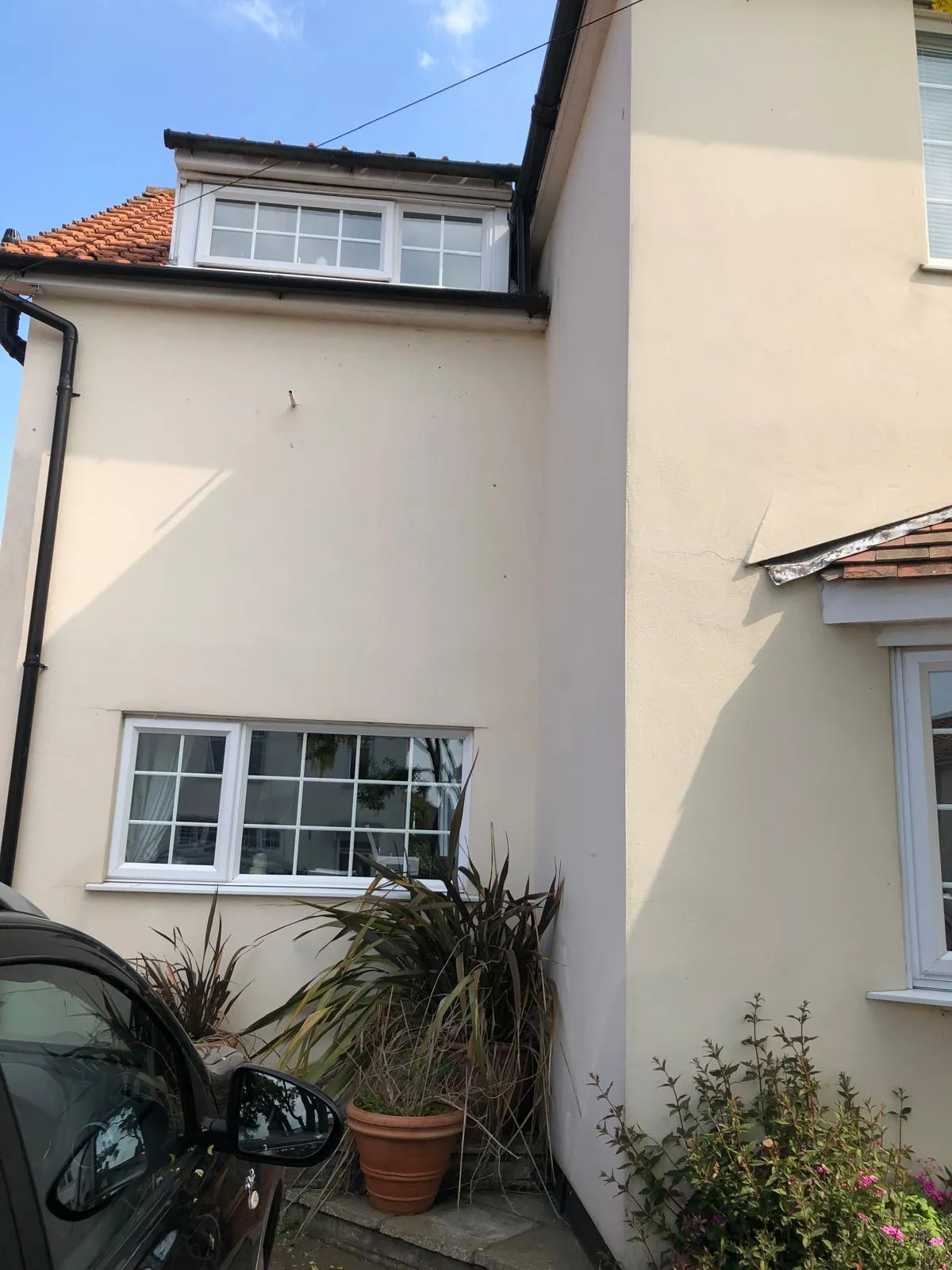 Cream rendered house exterior with white uPVC windows, a dormer conversion, and black guttering.