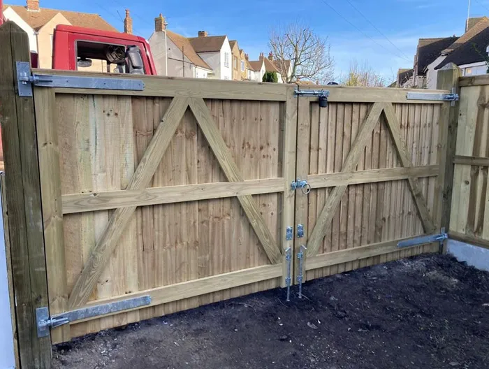A close-up of a new double wooden driveway gate, showing the sturdy timber construction, diagonal bracing, and heavy-duty metal hardware.