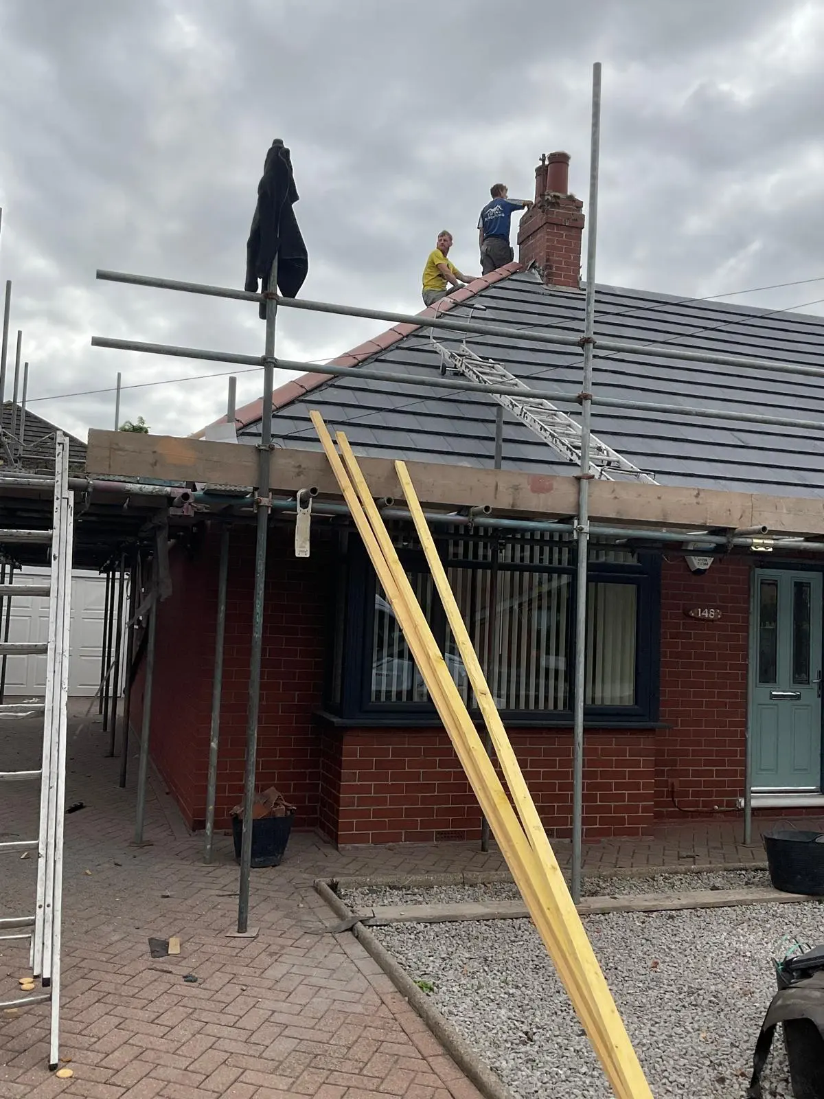 Professional roofers carrying out repairs on a residential tiled roof and chimney stack with scaffolding