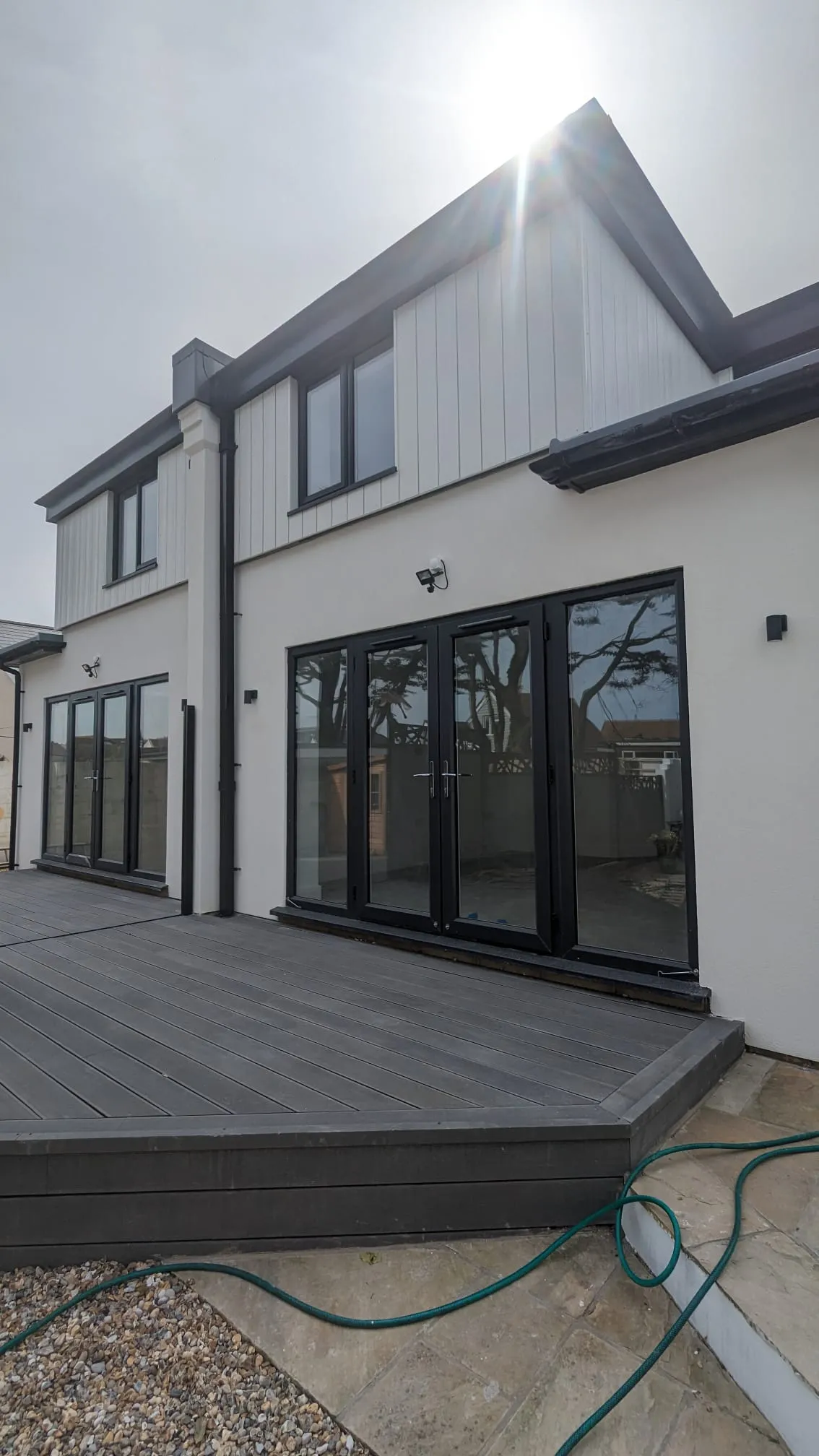 A house with fresh white external rendering and black bifold doors opening onto a grey deck.