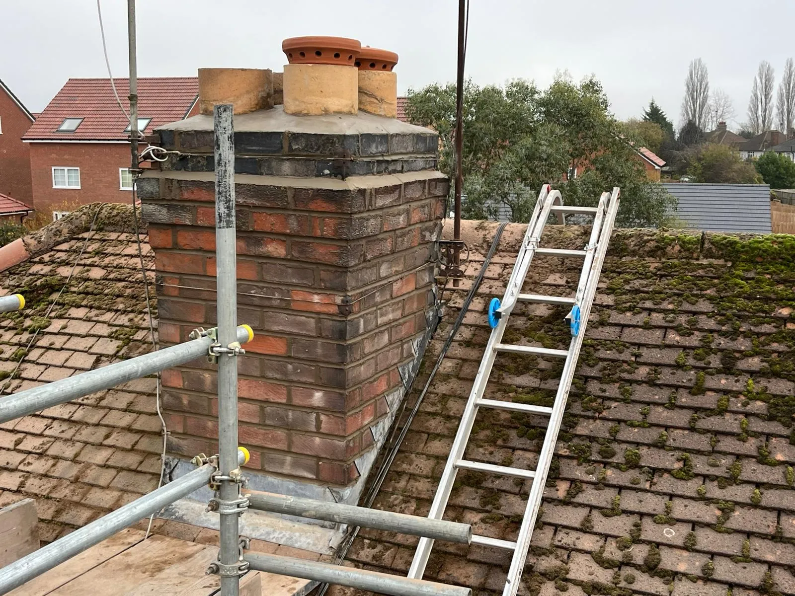 Chimney repairs and maintenance on a residential roof in Gloucestershire with scaffolding and roof ladder