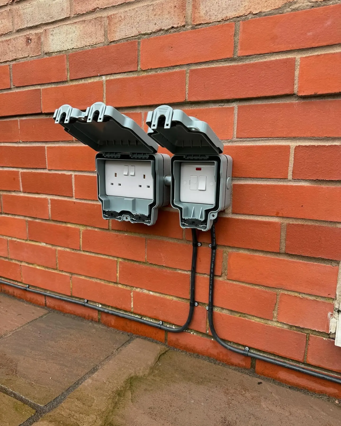 Weatherproof outdoor double socket and switch installation on a red brick wall