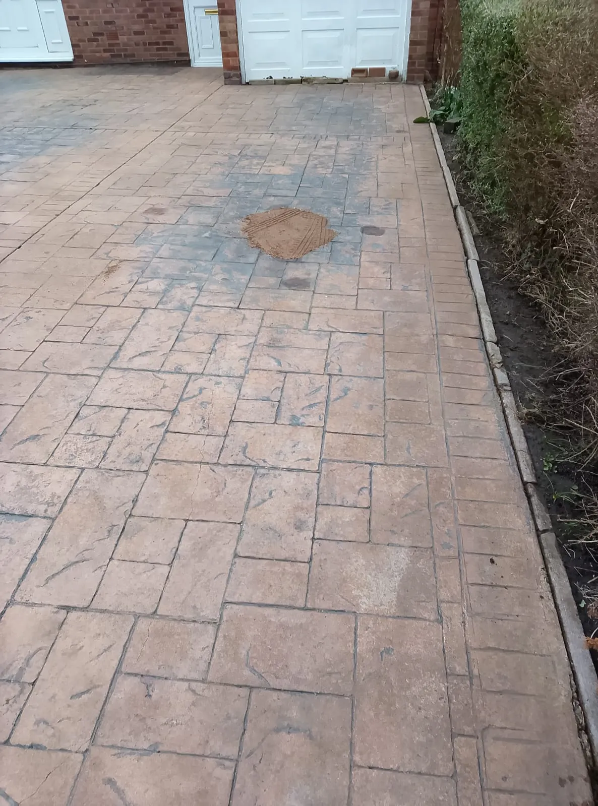 A patterned concrete driveway with a small pile of sand in the centre, indicating maintenance or repair work.