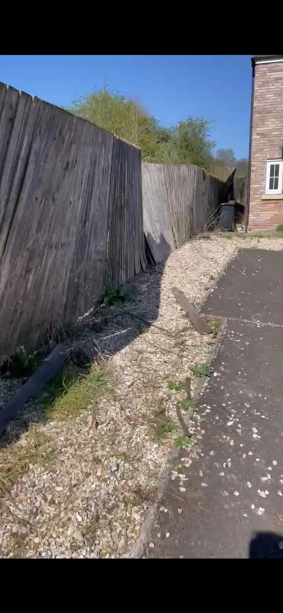 Storm-damaged timber garden fence leaning and in need of post repair and replacement