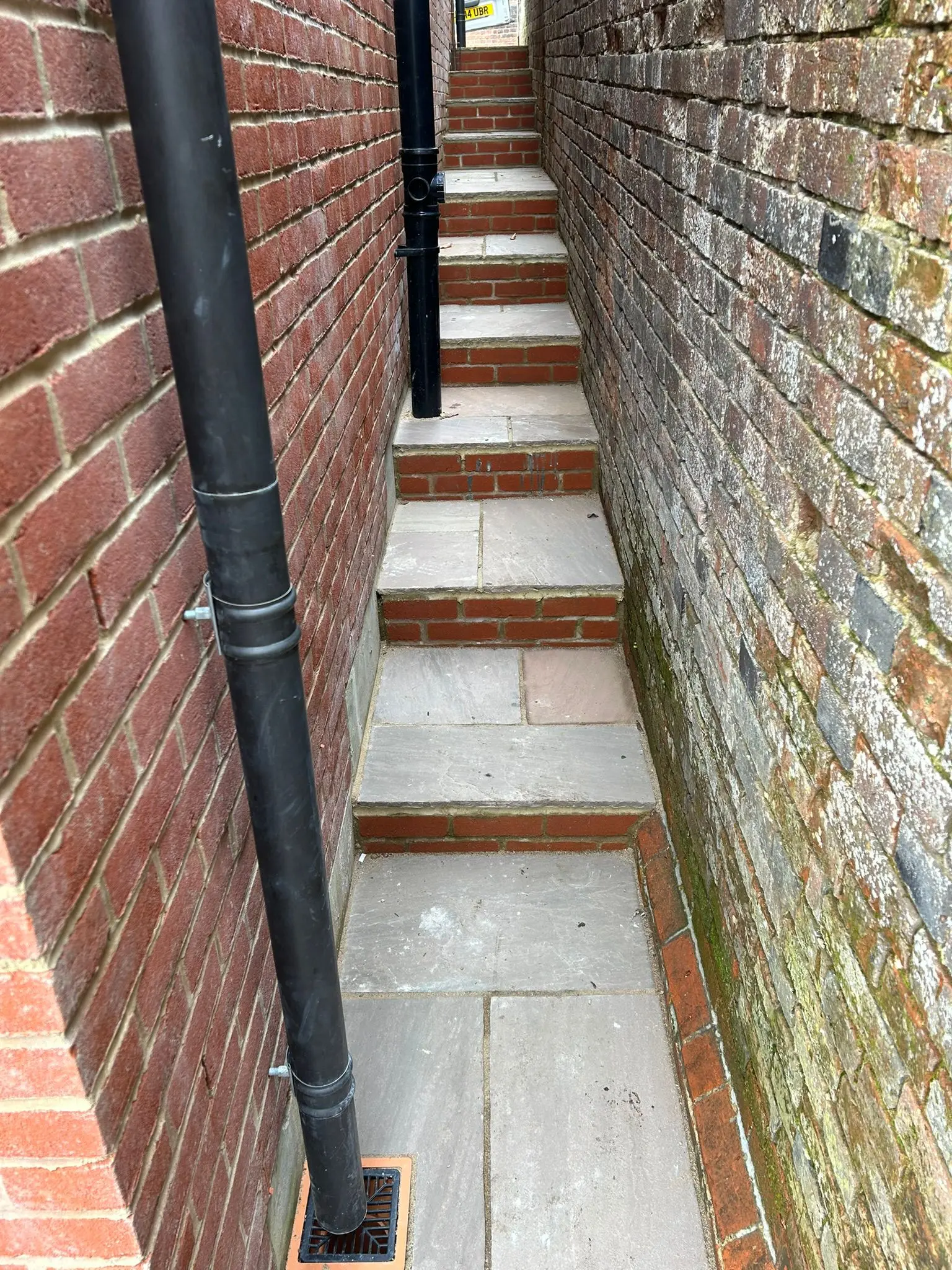 Natural stone paving and brick step risers installed in a narrow side passageway, showcasing expert hard landscaping and brickwork.