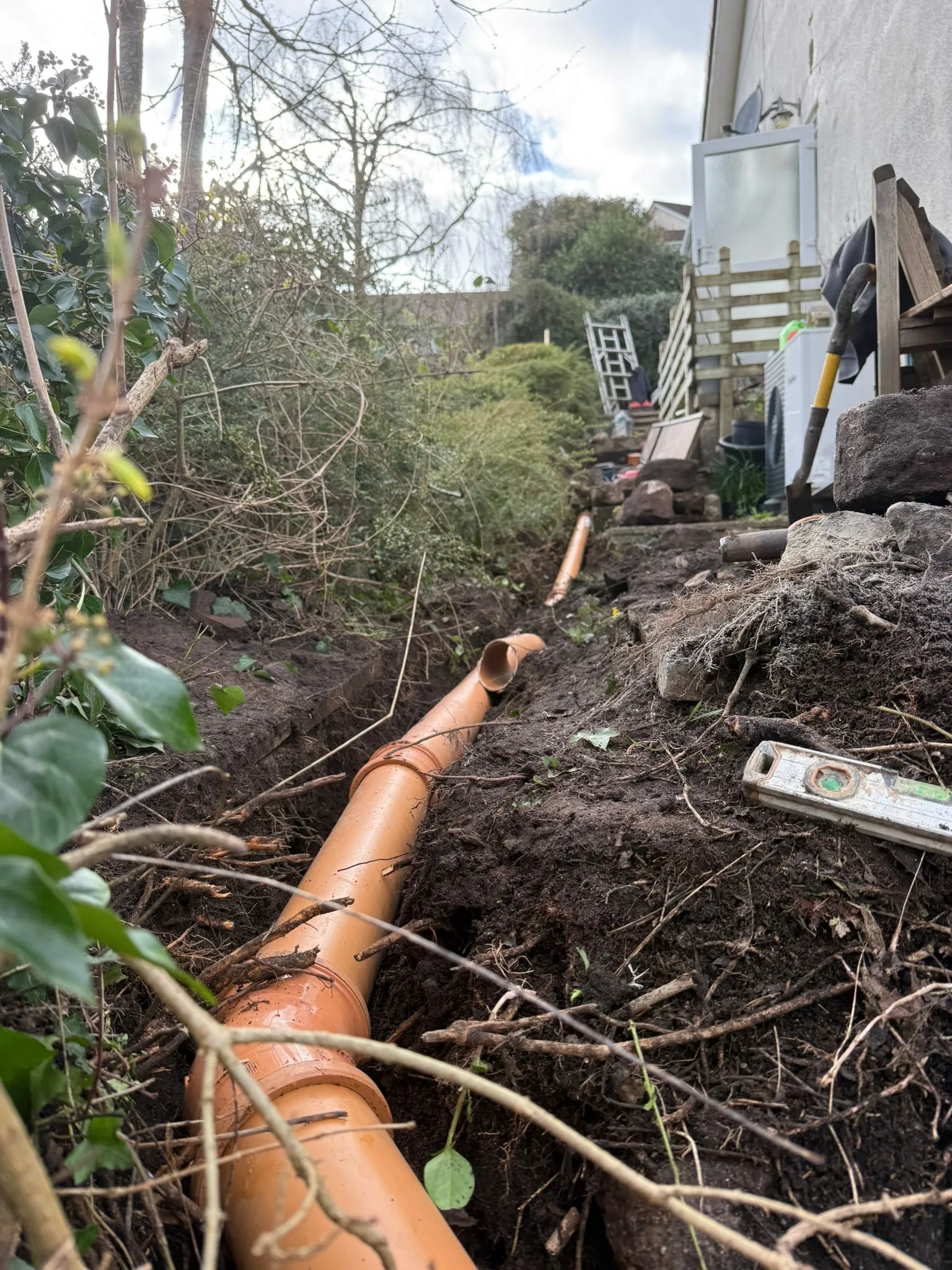 New orange drainage pipes being installed in a garden trench by Drainage South Ltd in Bournemouth.