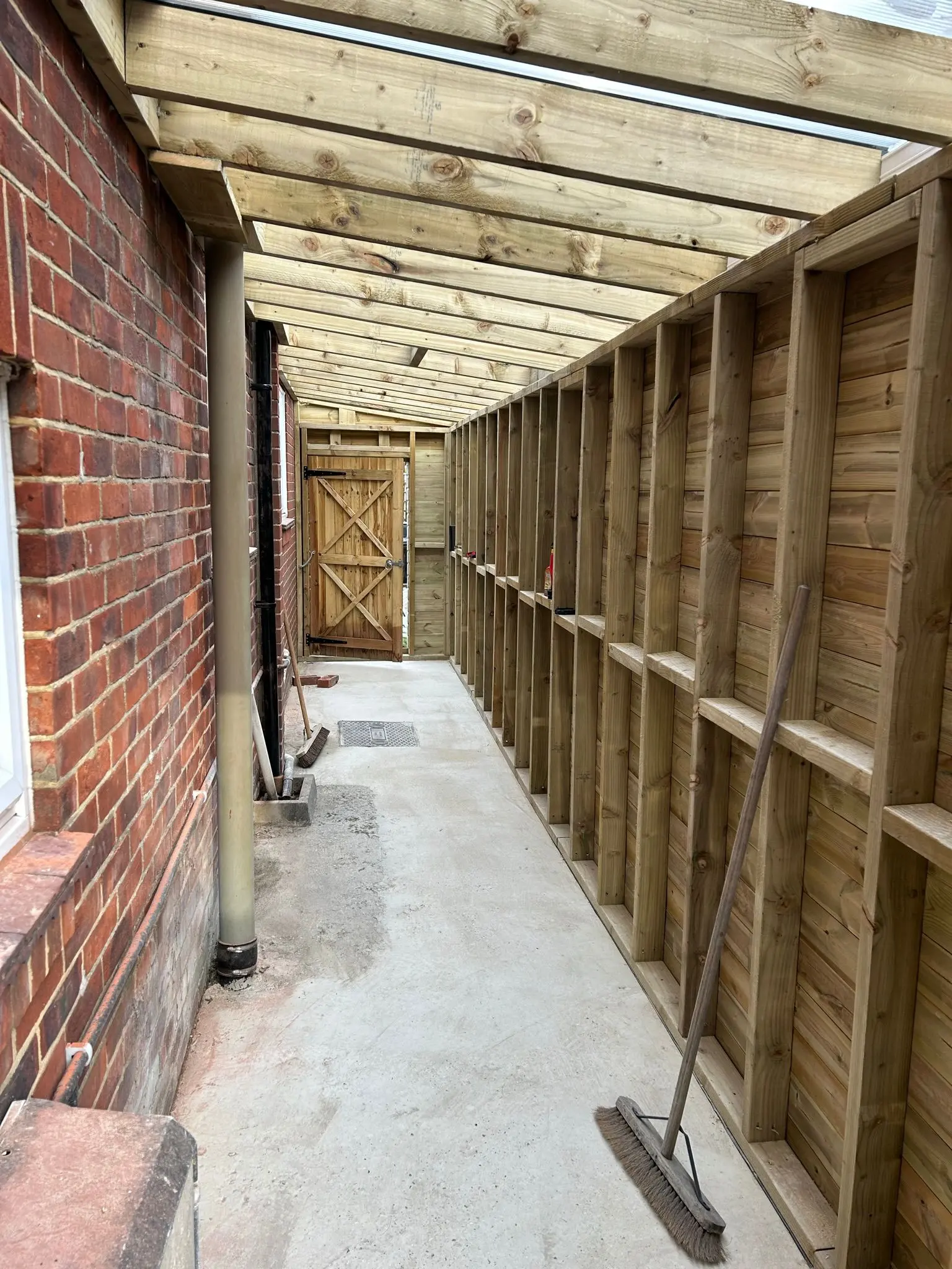 Timber-framed side return extension and covered walkway under construction alongside a brick house by Aline Construction