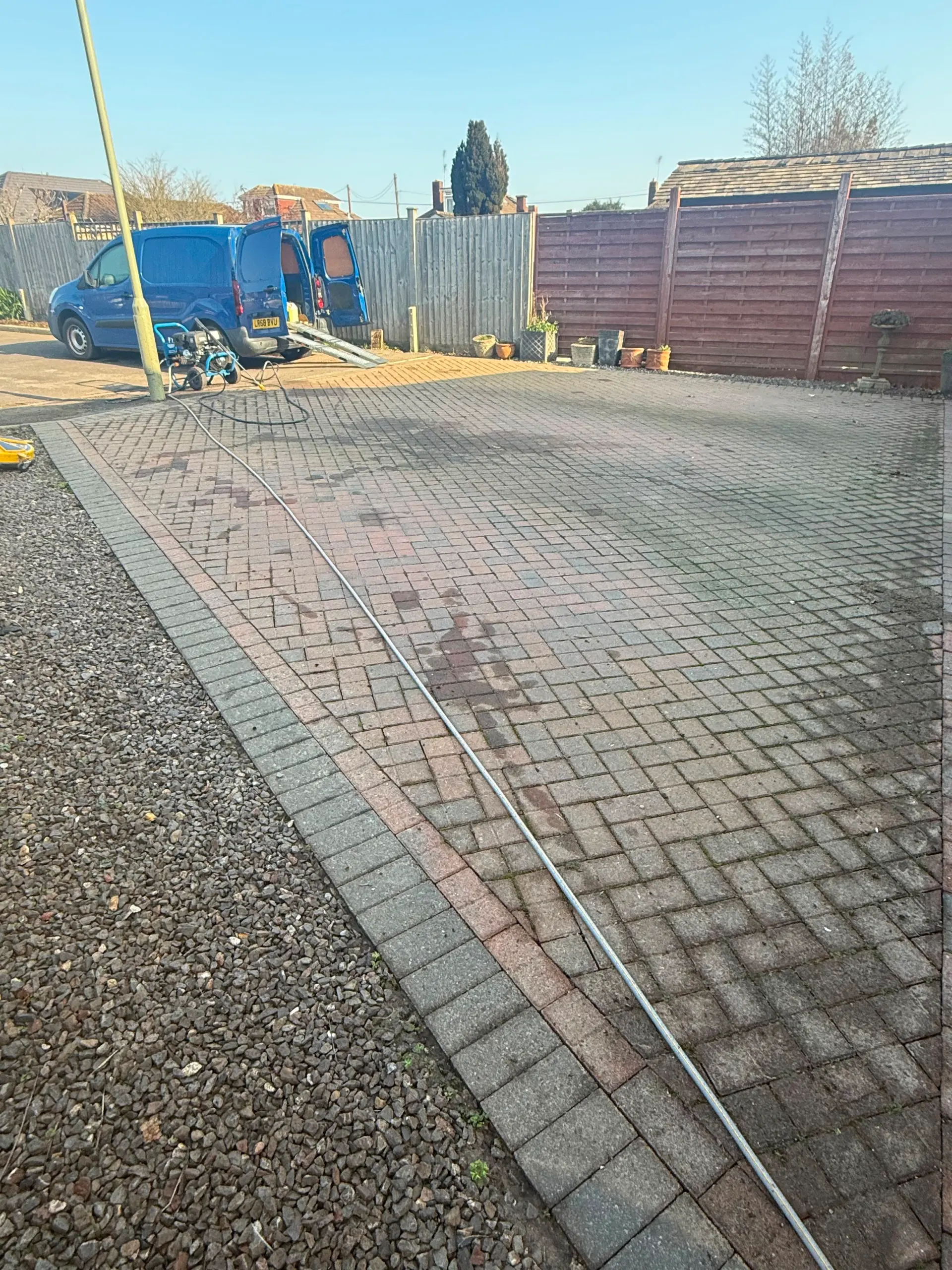 Block paved driveway undergoing professional pressure washing with van and equipment.