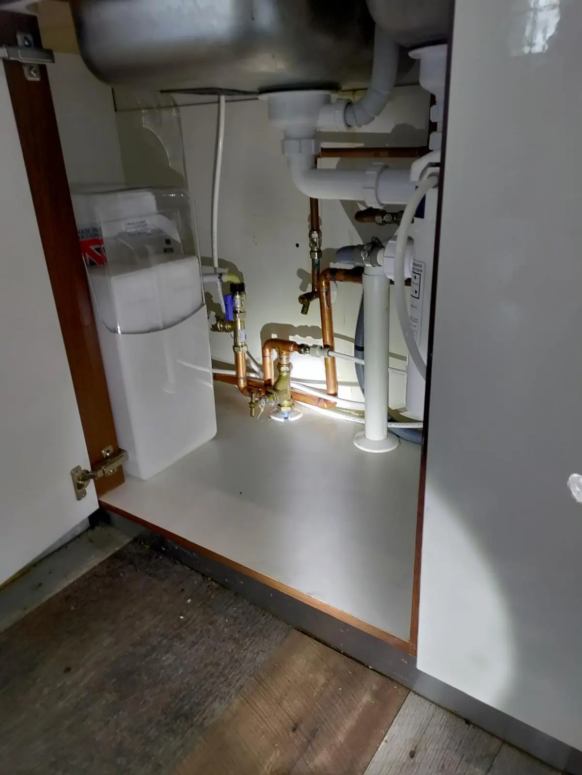 Kitchen plumbing under a sink showing copper pipes and white waste pipes in Frome