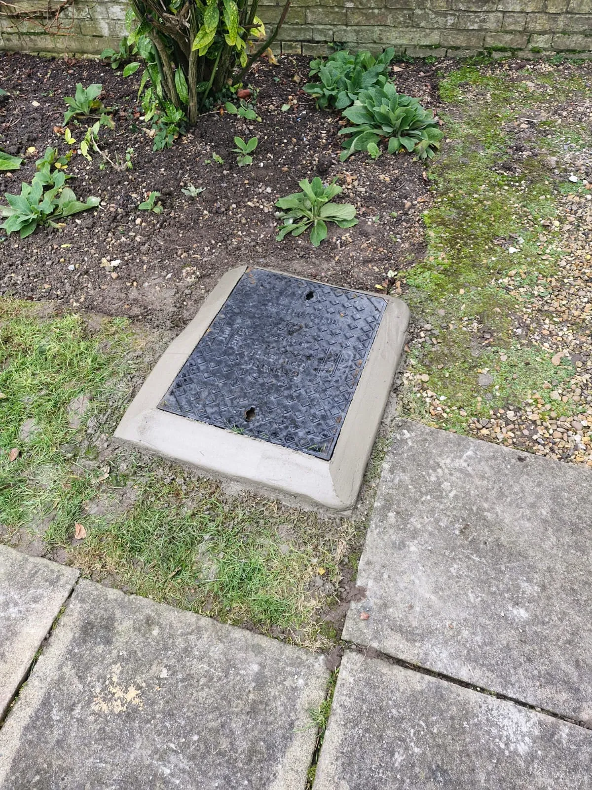 A professionally repaired and concreted manhole cover in a garden by Roberts Drainage Ltd.