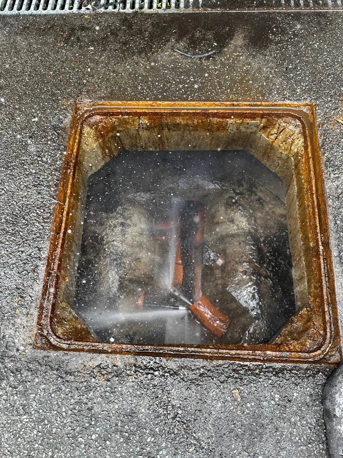 A professional using high-pressure water jetting to unblock an outdoor drain.
