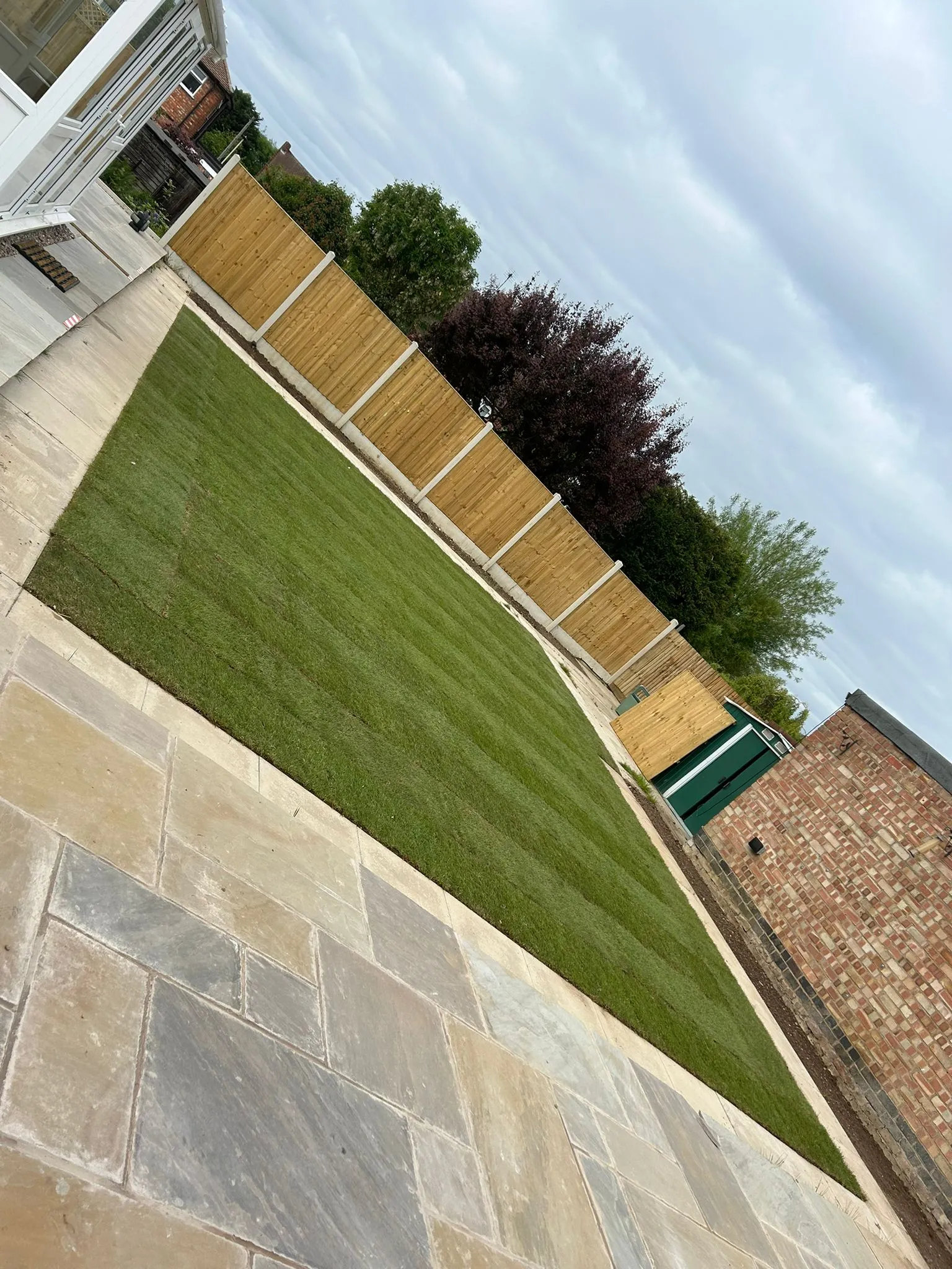A modern, freshly landscaped garden with a natural stone patio and a new green lawn bordered by a timber fence.