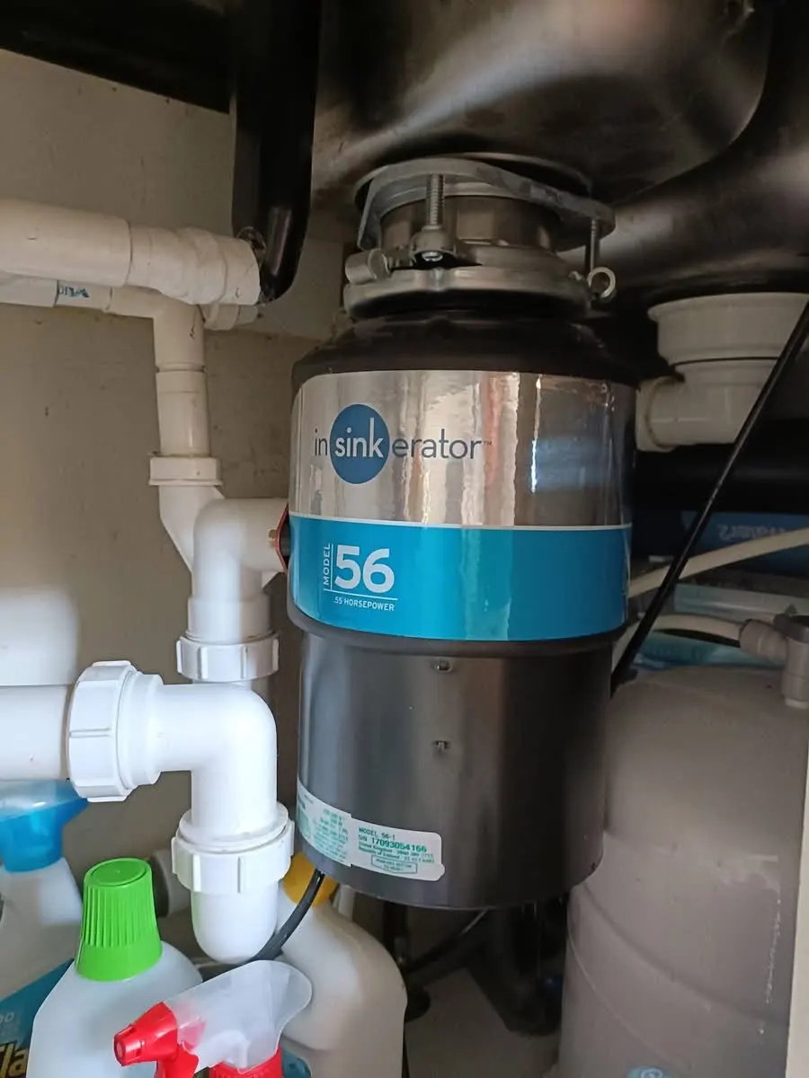 An InSinkErator waste disposal unit and connected plumbing pipes installed under a kitchen sink.