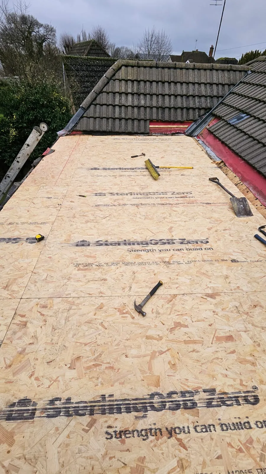 Roof under construction with OSB boards laid, showing preparation for a new flat roof installation alongside existing pitched roofs.