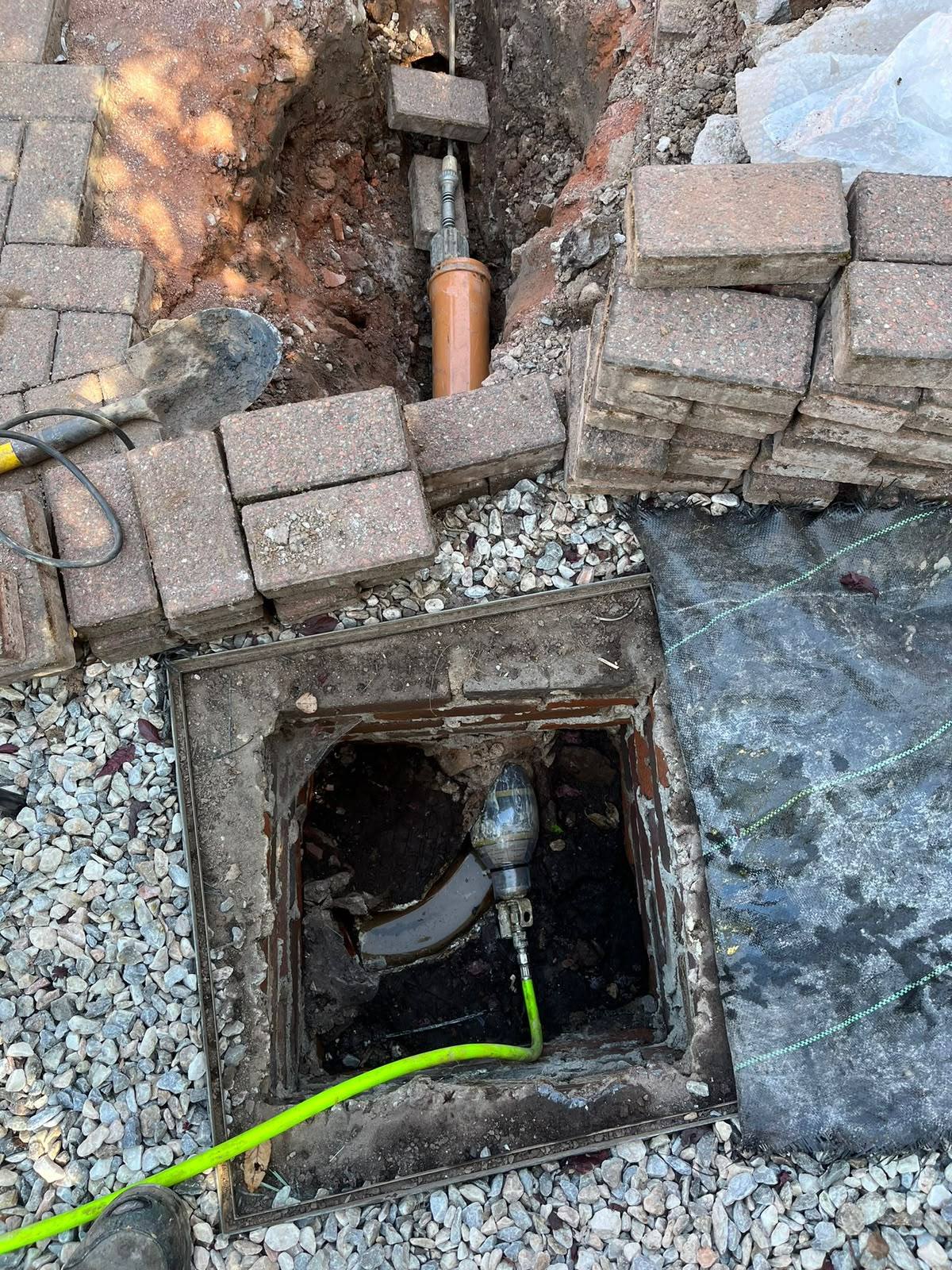 Drainage excavation and high-pressure water jetting equipment clearing a blocked pipe via an open manhole