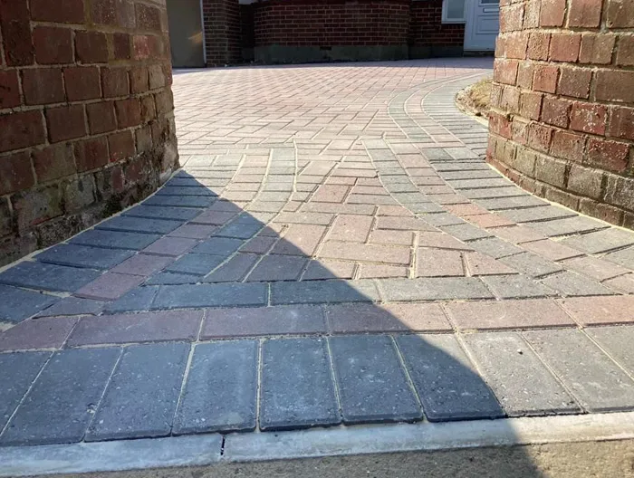 Newly laid block paving driveway with a curved design, bordered by brick walls, showcasing grey and red paving blocks under partial sunlight.