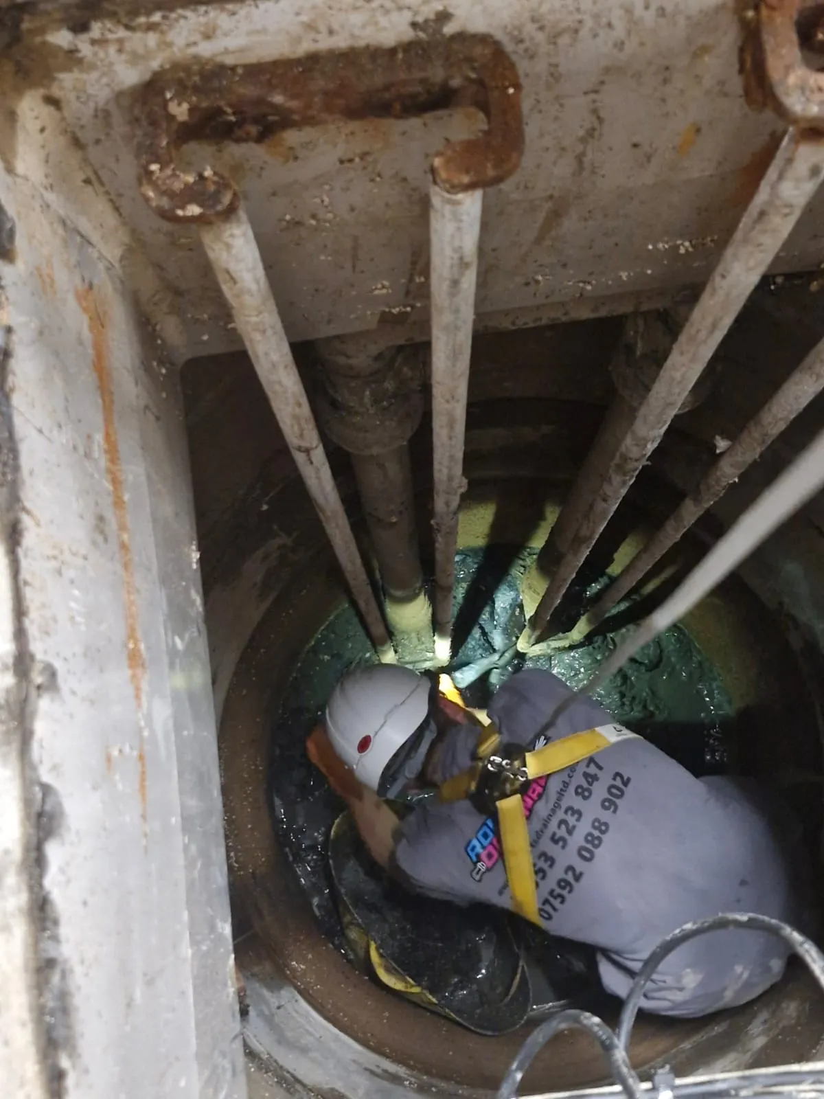 Professional drainage engineer performing pump station maintenance inside a deep chamber.