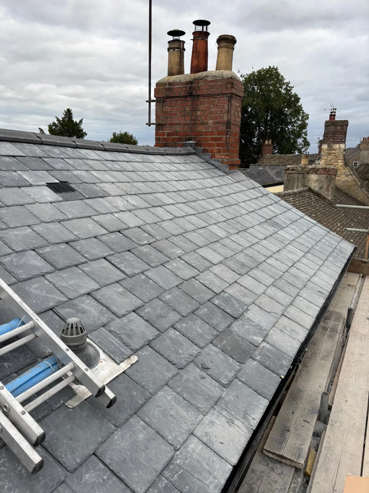 Close-up of a freshly installed grey slate roof and a brick chimney stack, showcasing high-quality re-roofing work by Delta Roofcare Ltd.