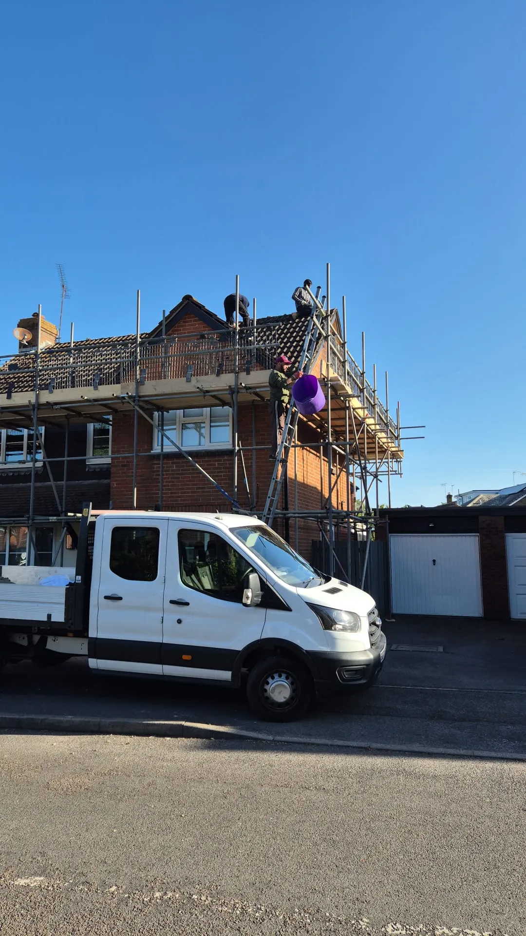 Roofers from Watertight Roofing working on a house roof with scaffolding and a white company van in Portsmouth