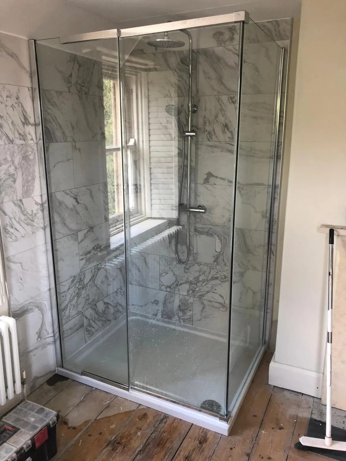 A professionally installed glass shower cubicle with marble-effect tiling and a thermostatic mixer valve, showcasing high-quality bathroom plumbing by BC Plumbing.