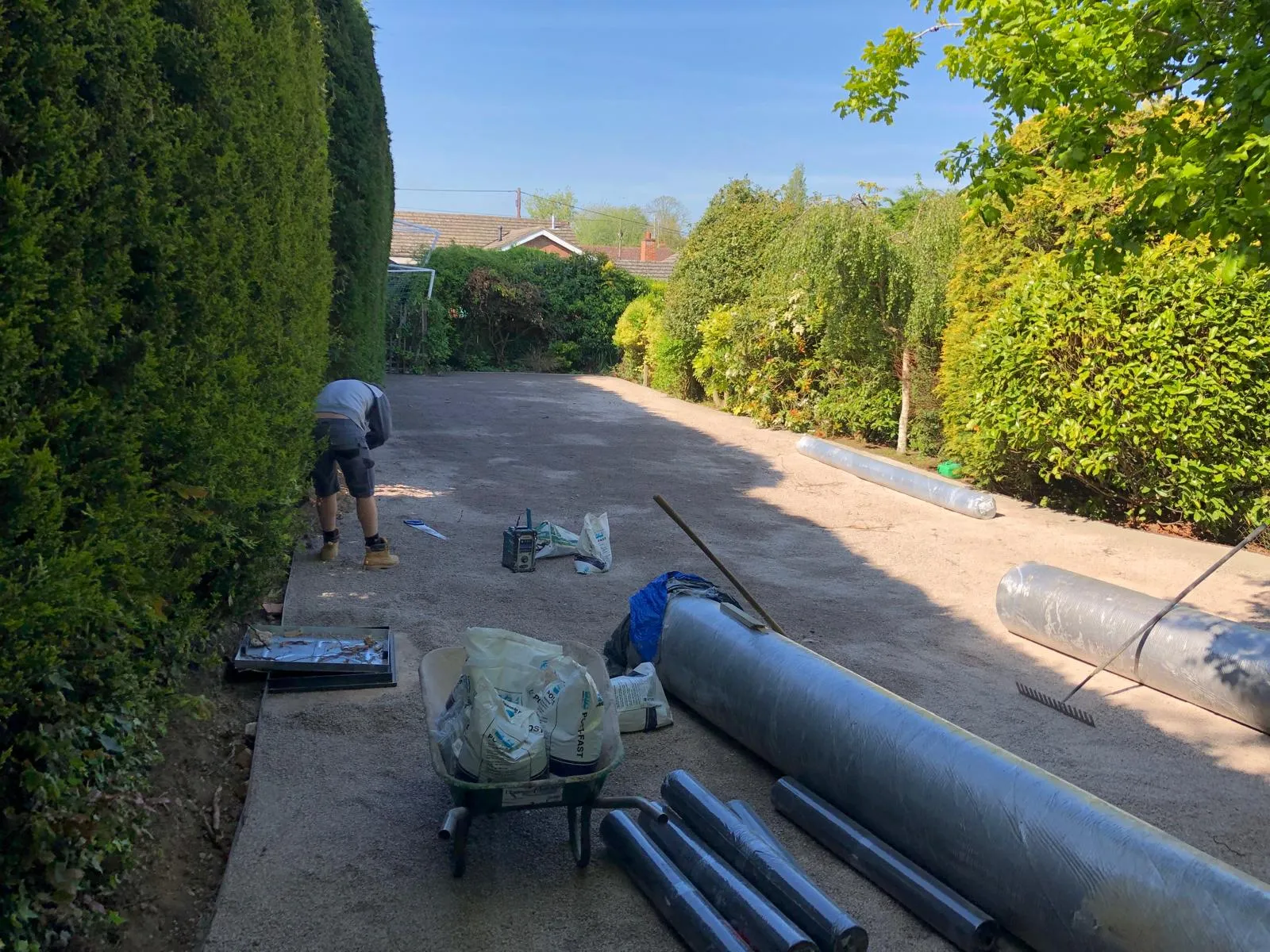Groundwork for a new driveway, with a worker, prepared sub-base, and rolls of membrane ready for installation.