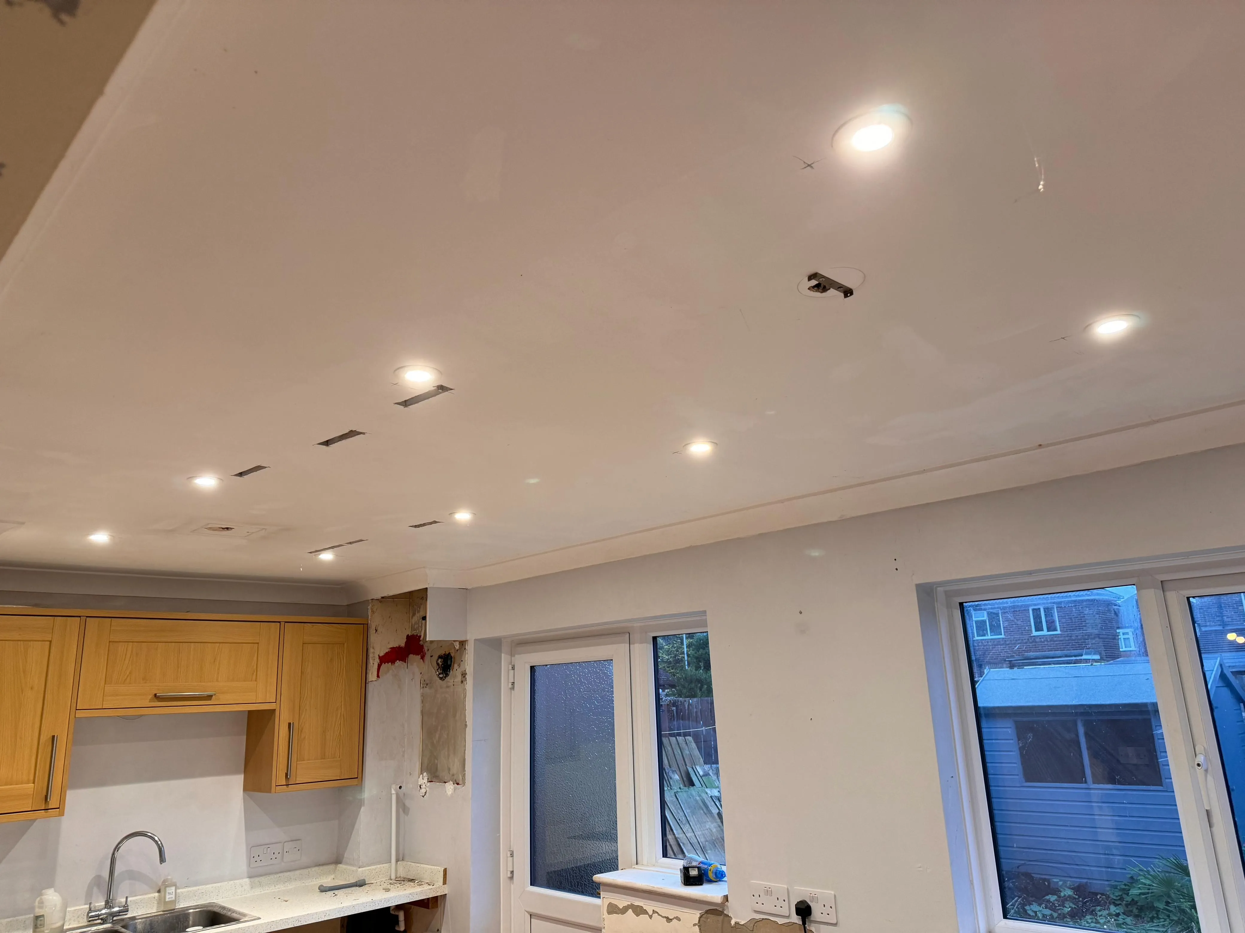Electricians installing recessed LED spotlights in a kitchen ceiling during a renovation