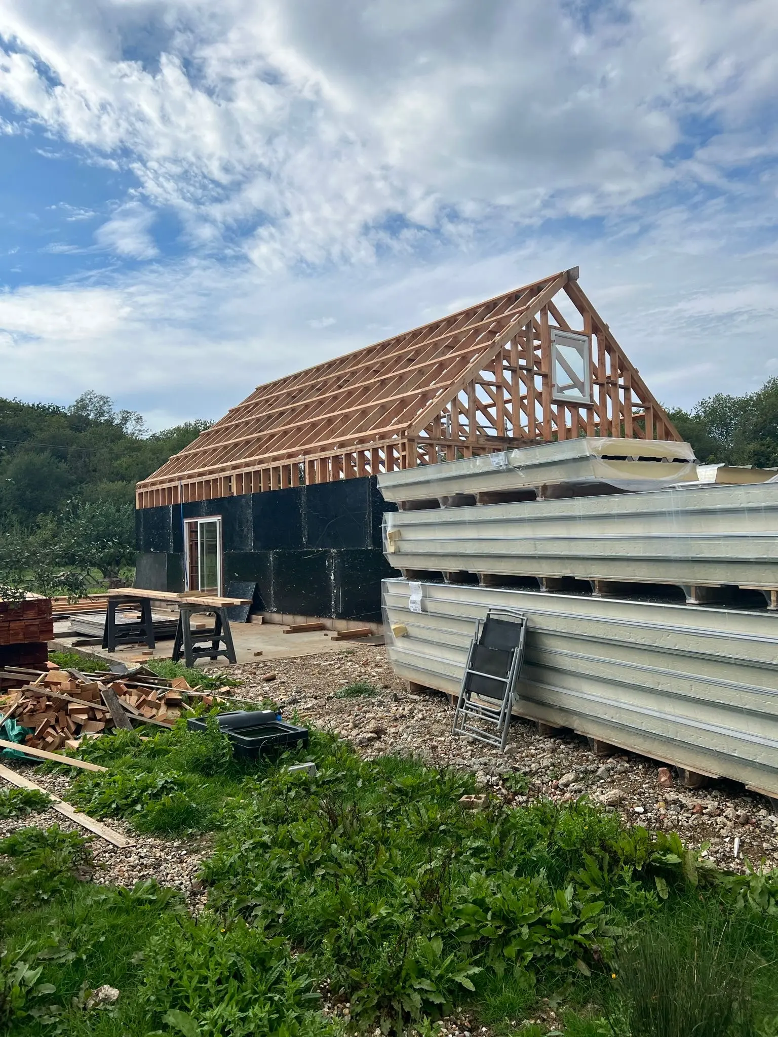 Agricultural shed construction in progress showing an exposed roof frame and stacks of weather-resistant cladding panels waiting to be installed.