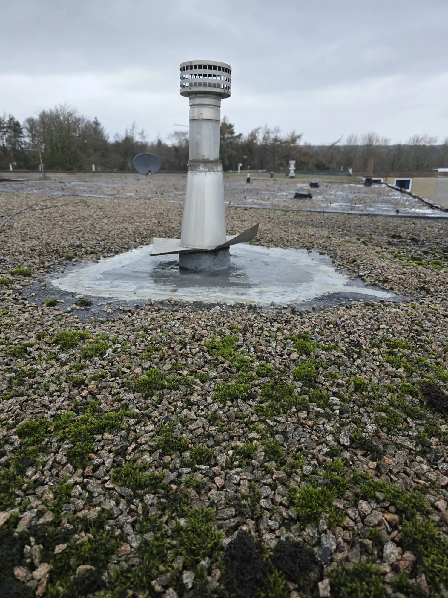 A repaired metal flue pipe on a flat roof with fresh waterproofing sealant applied to prevent leaks