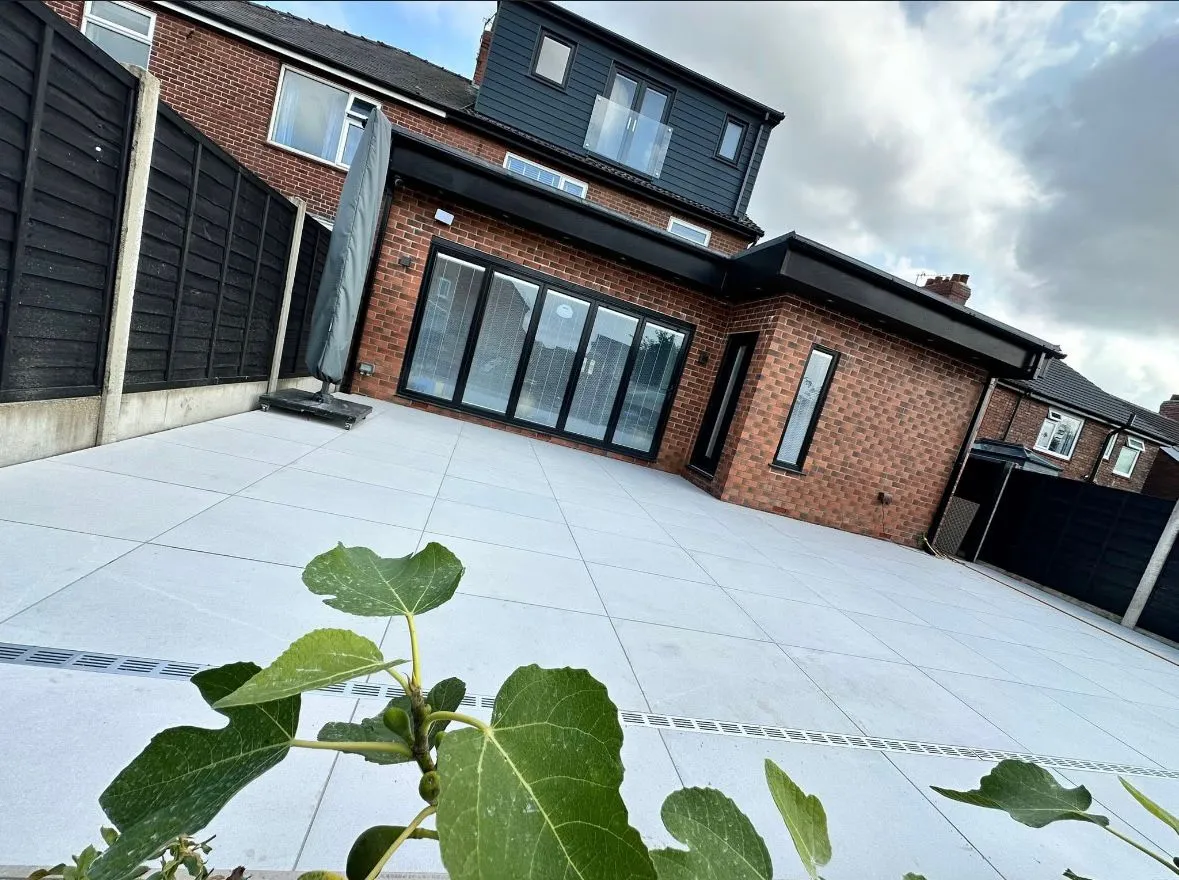 Modern porcelain paving patio with integrated drainage channel behind a brick house in Essex.