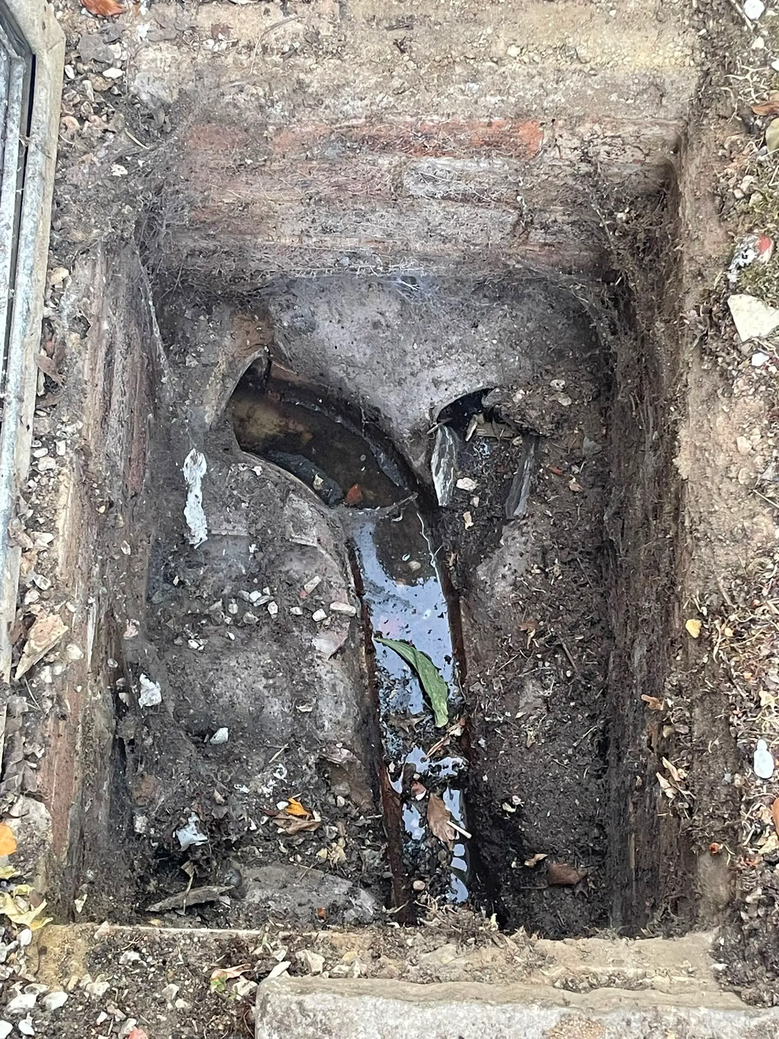 A close-up picture of a cracked and broken underground drainage pipe inside an open manhole inspection chamber