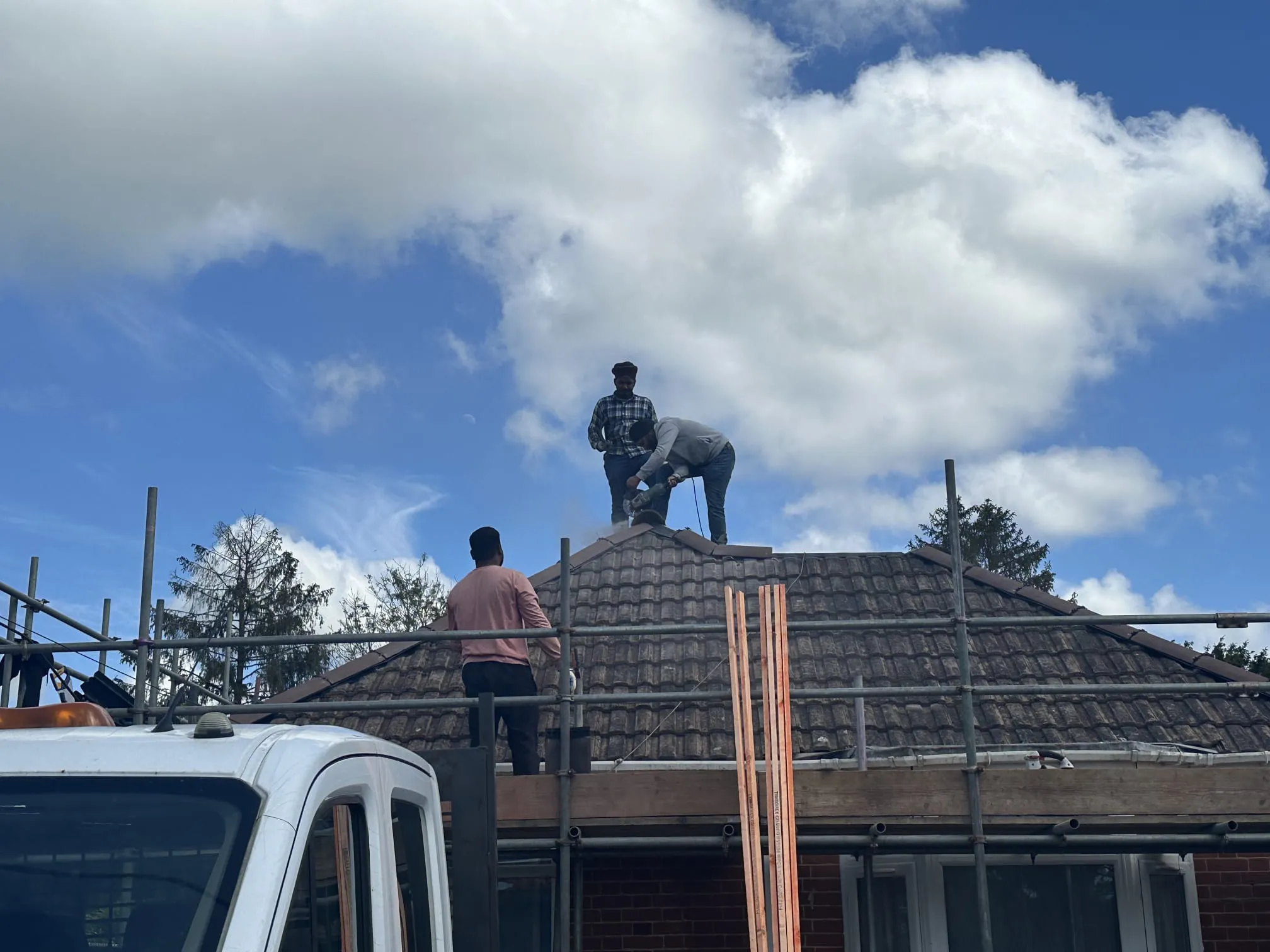 Roofers working on the ridge tiles of a pitched roof with scaffolding.