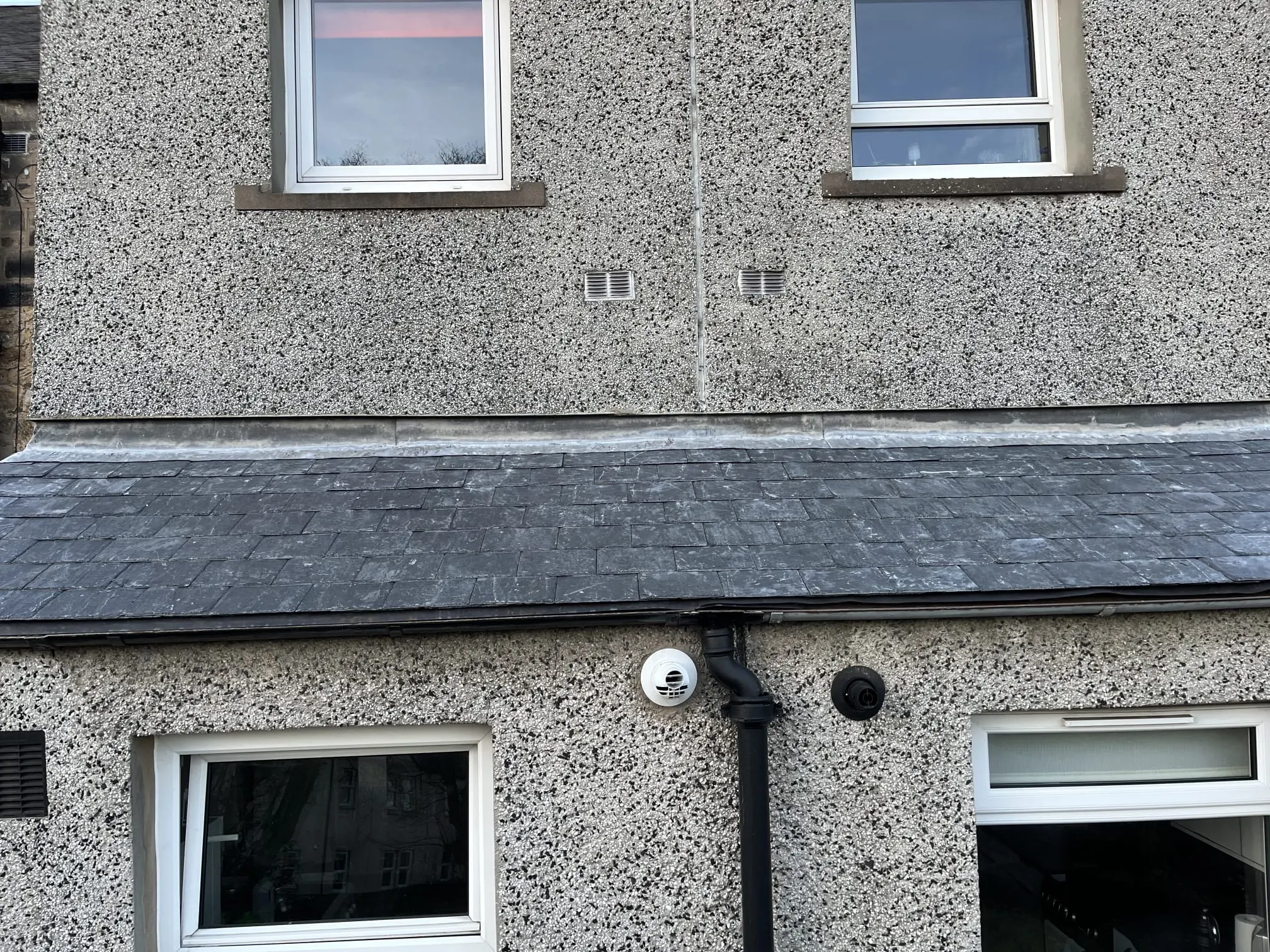 Exterior roughcast wall and slate roof section with lead flashing on a Scottish property