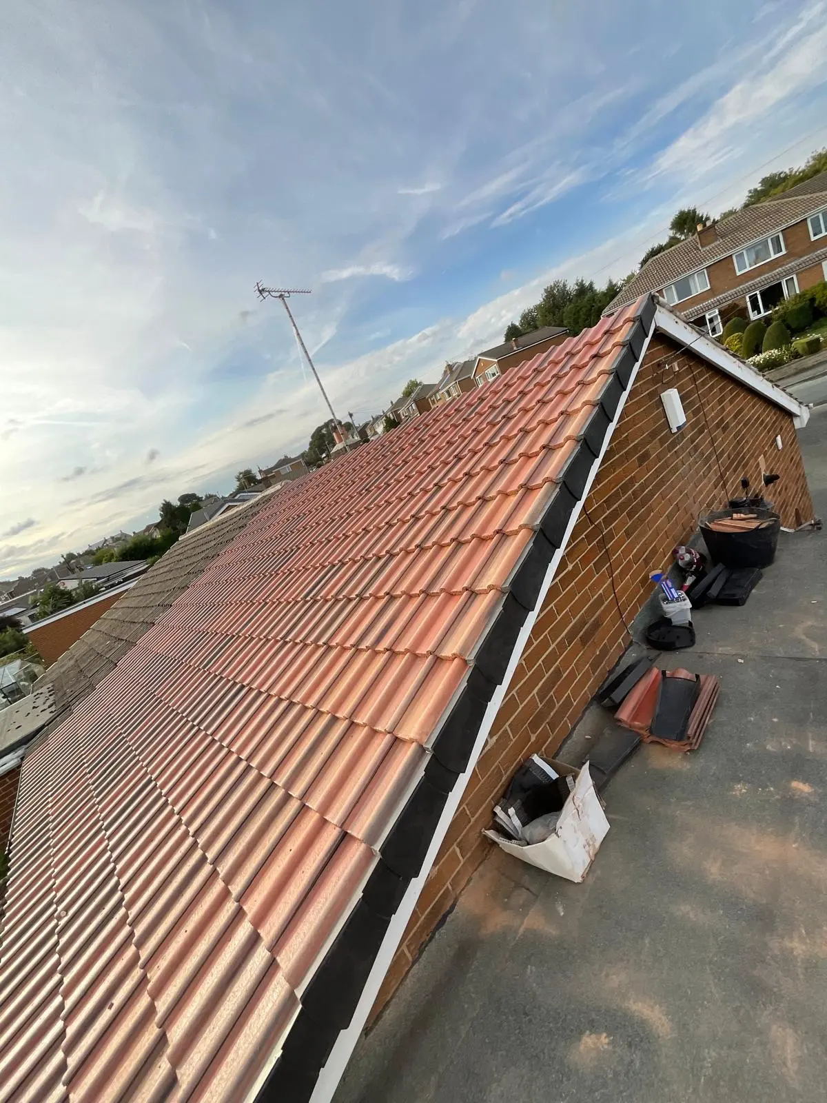 Newly tiled pitched roof with red-orange concrete tiles and black dry verge caps on a brick property