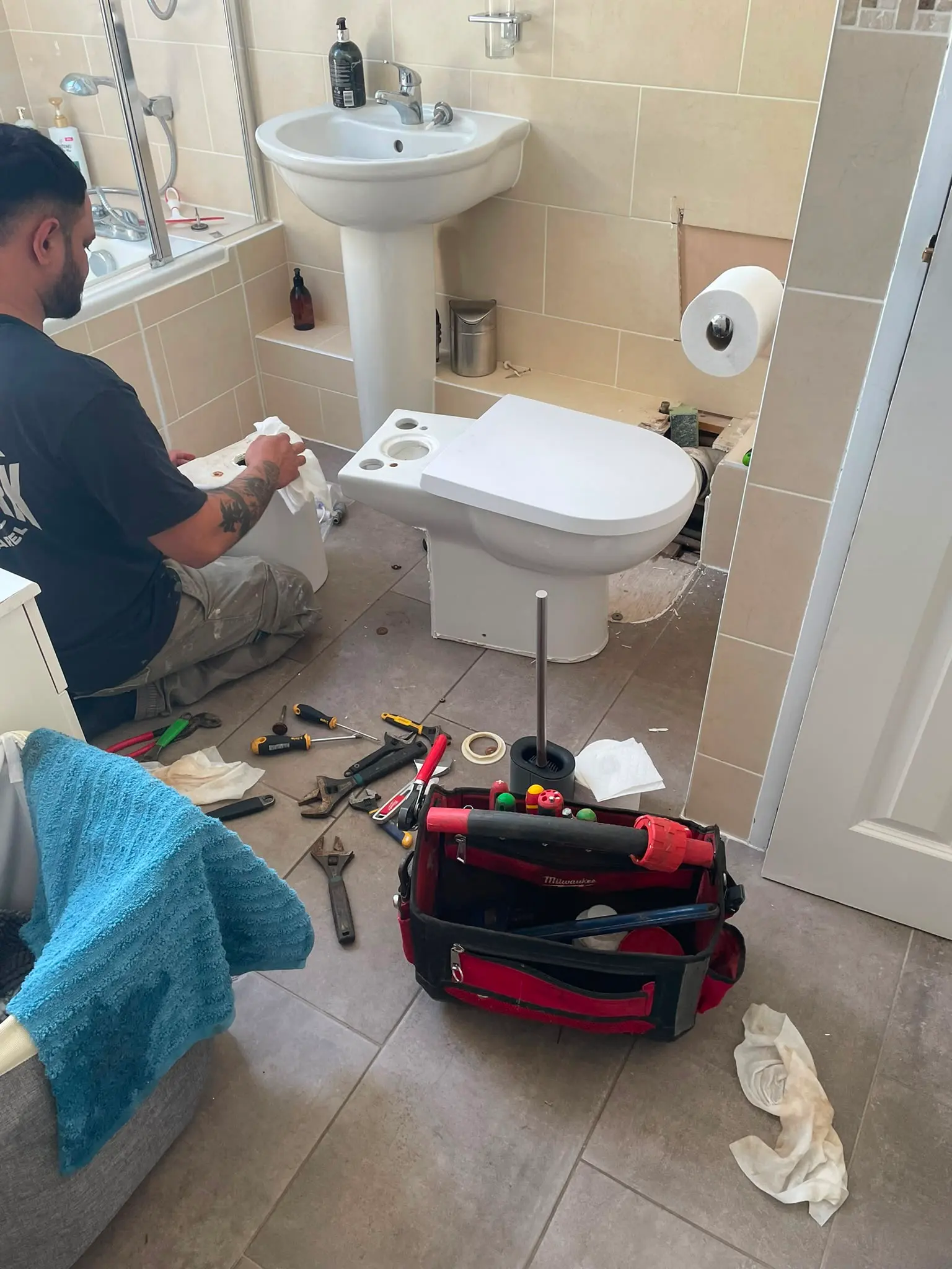 A professional plumber kneeling on a tiled bathroom floor, carrying out toilet repairs with a tool bag and wrenches scattered nearby