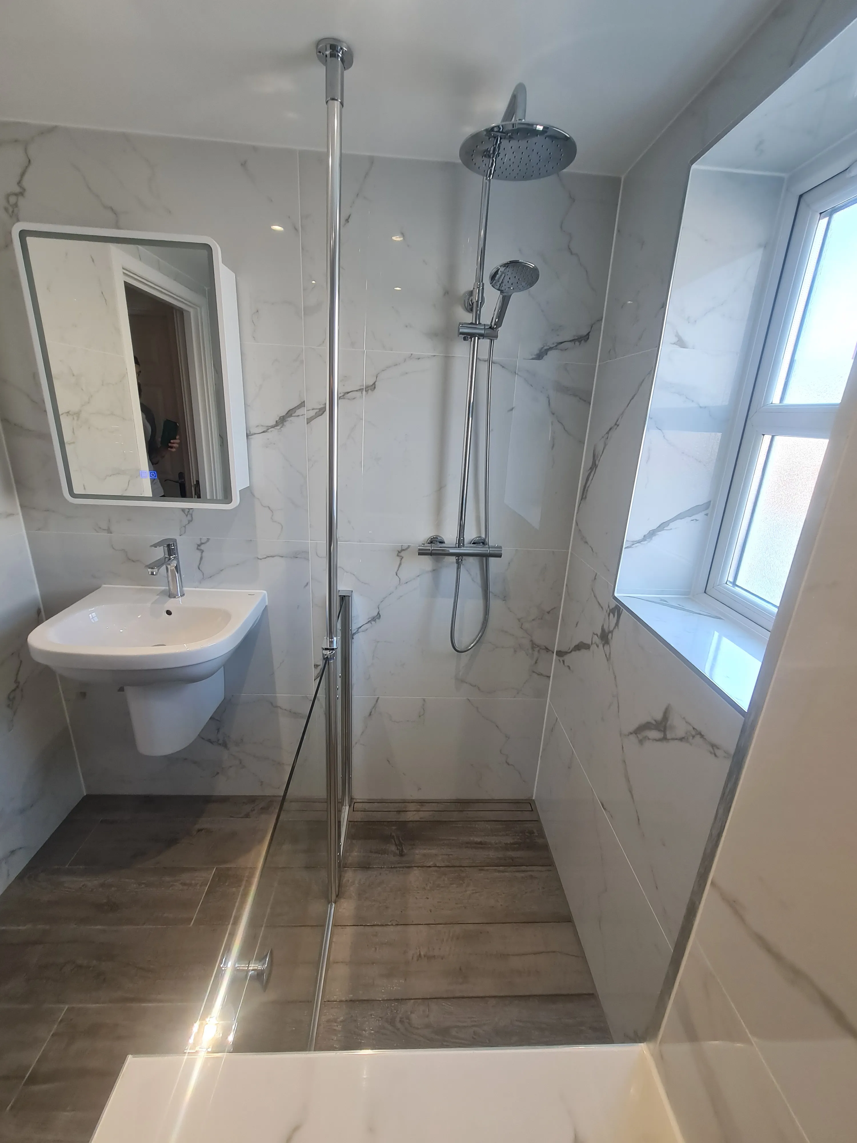 Bespoke luxury walk-in shower installation with marble-effect tiles and glass partition by Sands & Vossen in Plymouth.