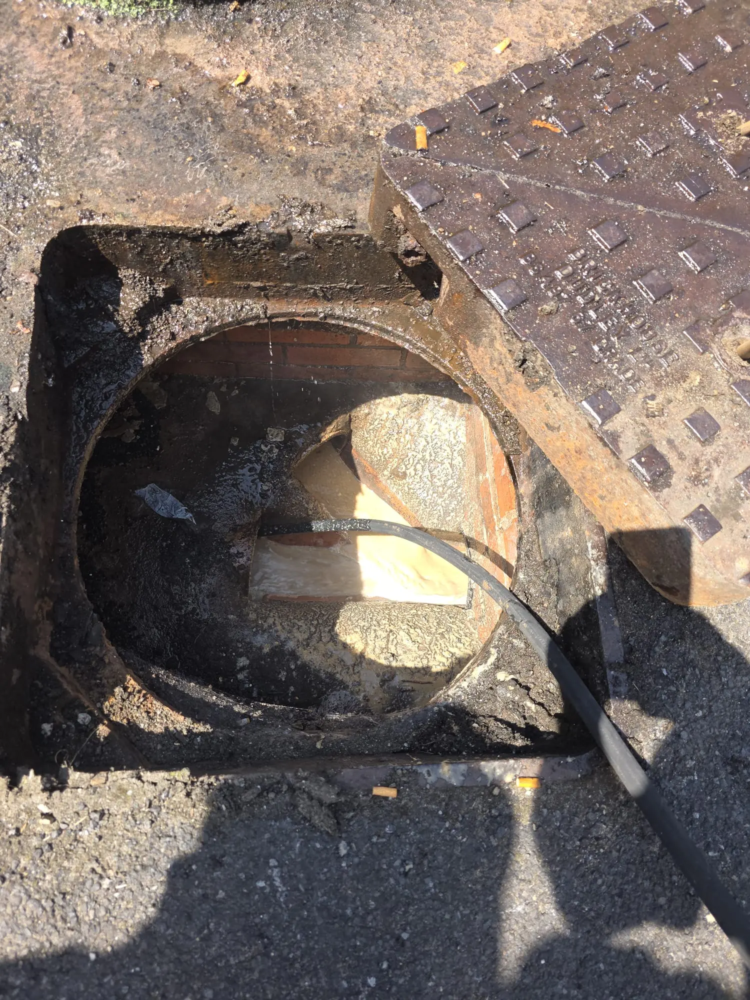 High-pressure water jetting hose clearing a blocked drain inspection chamber.