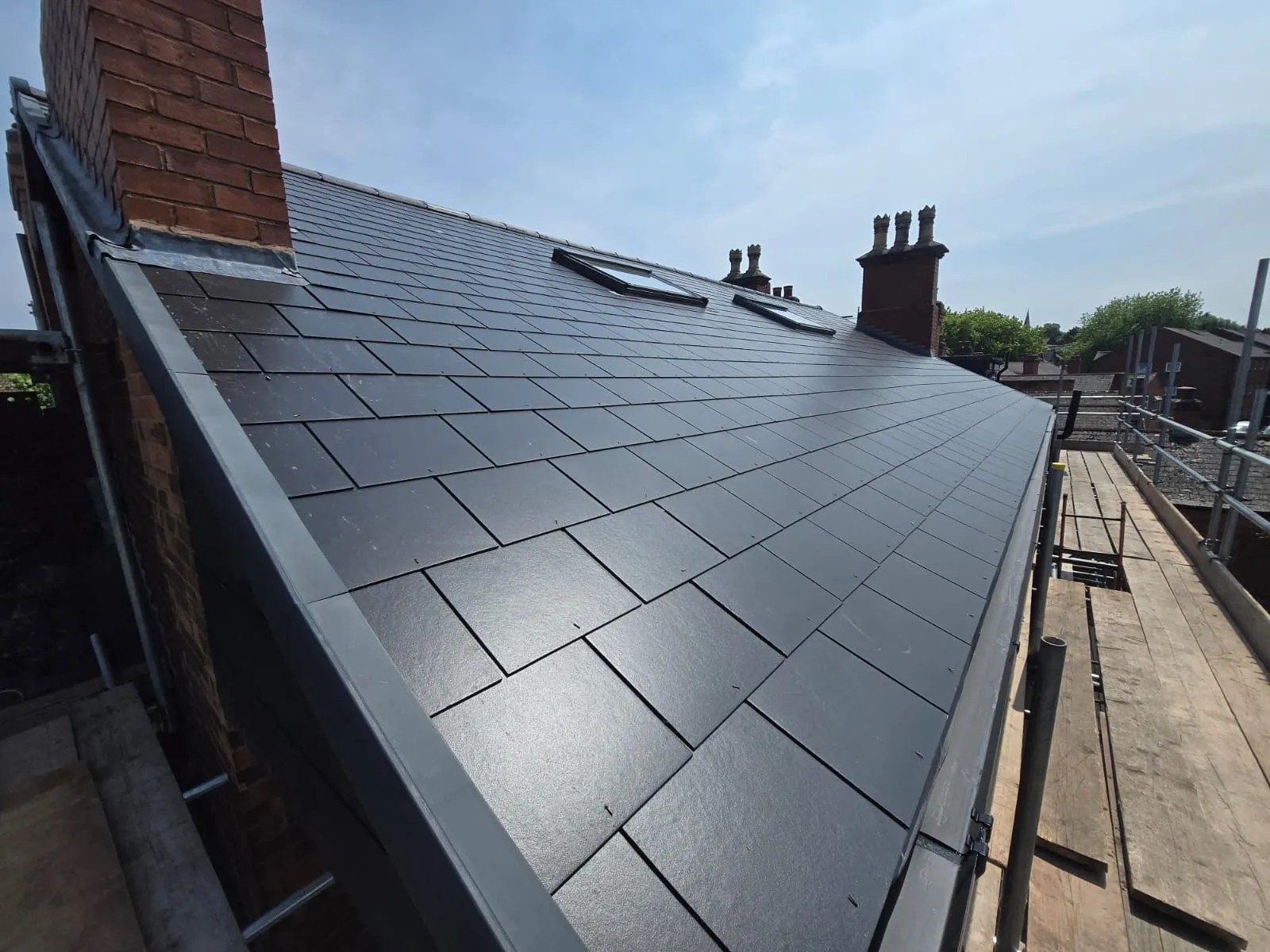 New dark grey tiled pitched roof with two roof windows and a brick chimney with lead flashing.