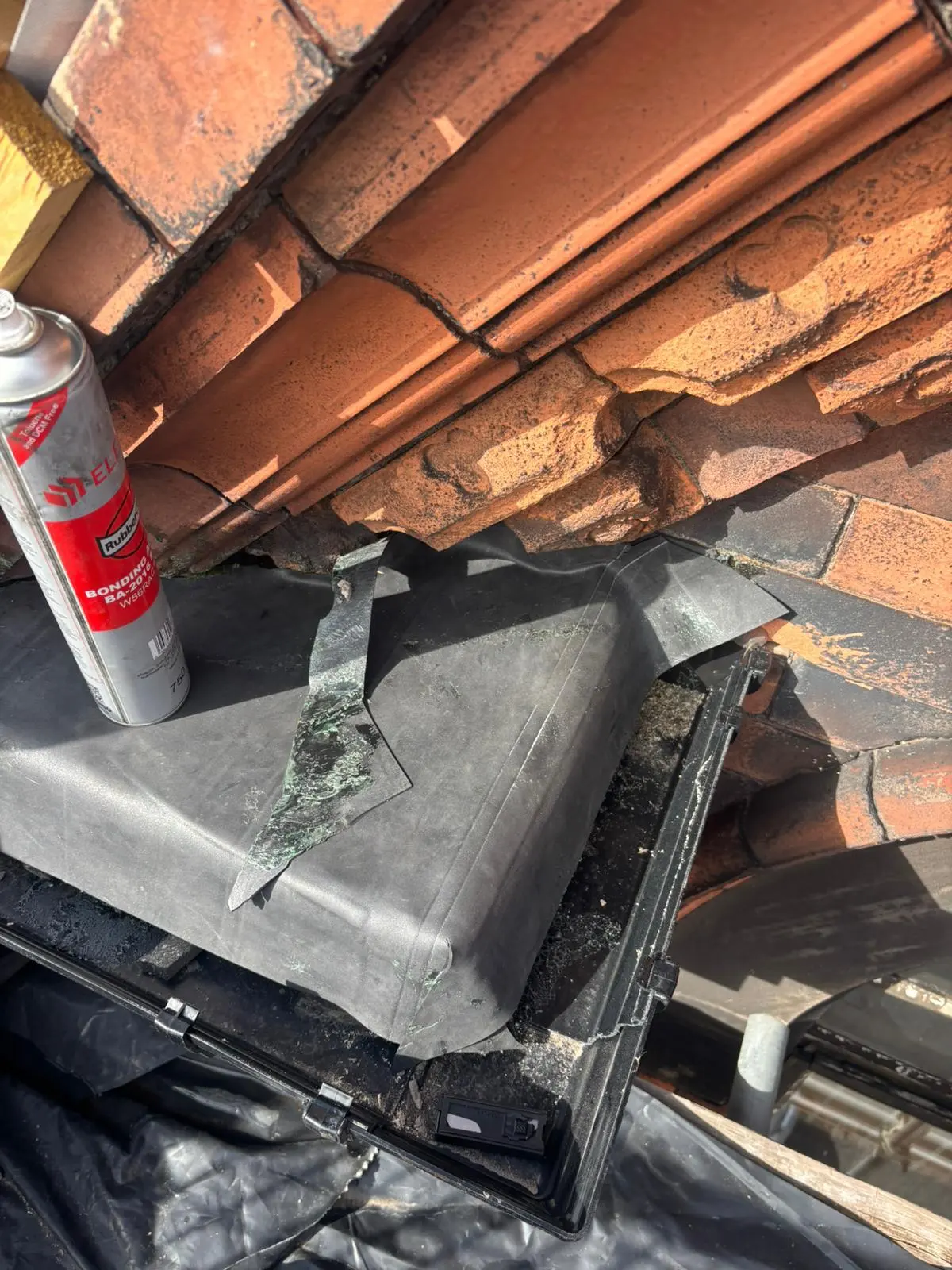 A close-up picture of roofing repair work showing flashing membrane and bonding adhesive on a tiled roof