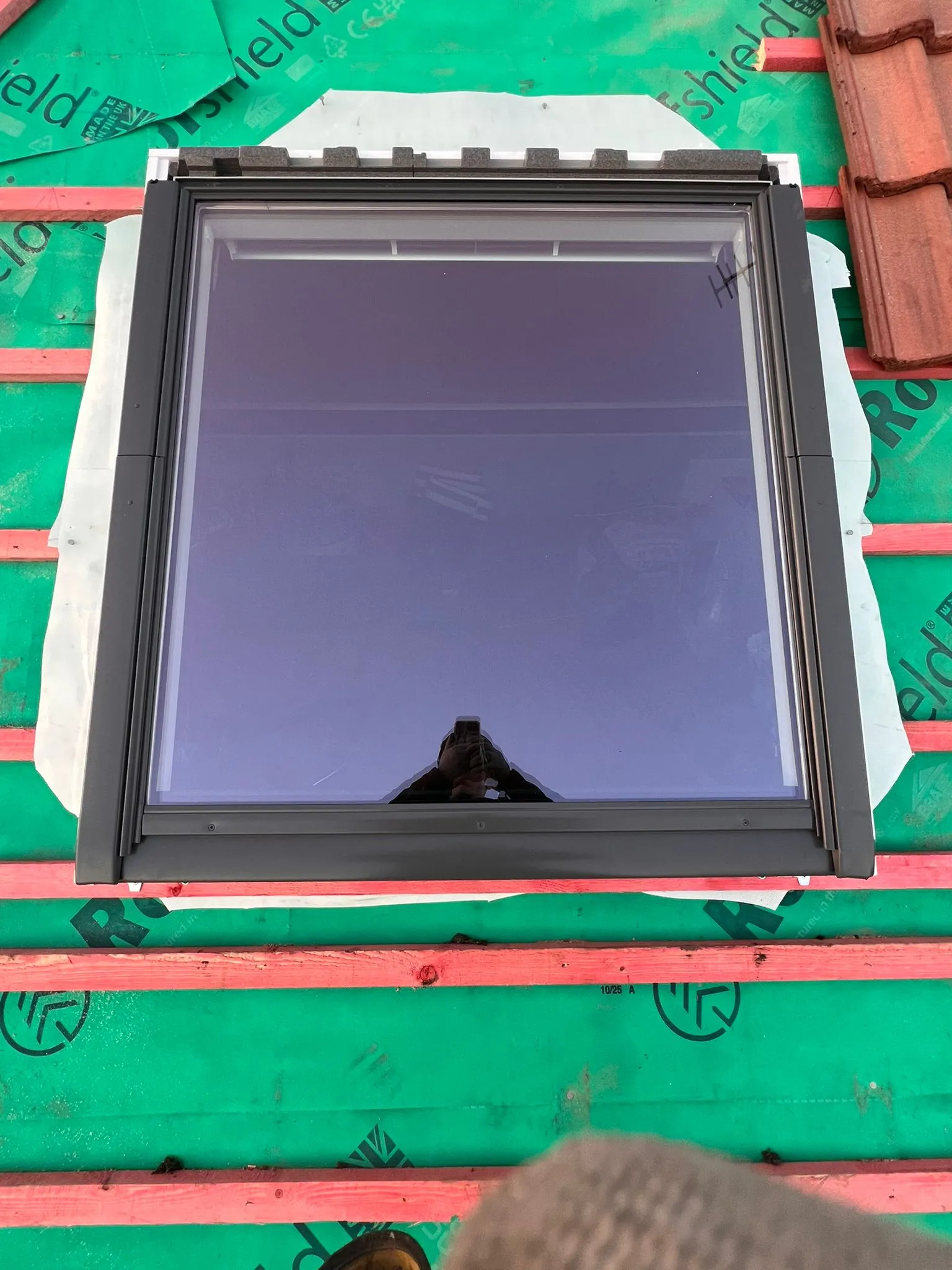 A Velux window being installed on a roof, showing the surrounding roofing membrane and wooden battens.