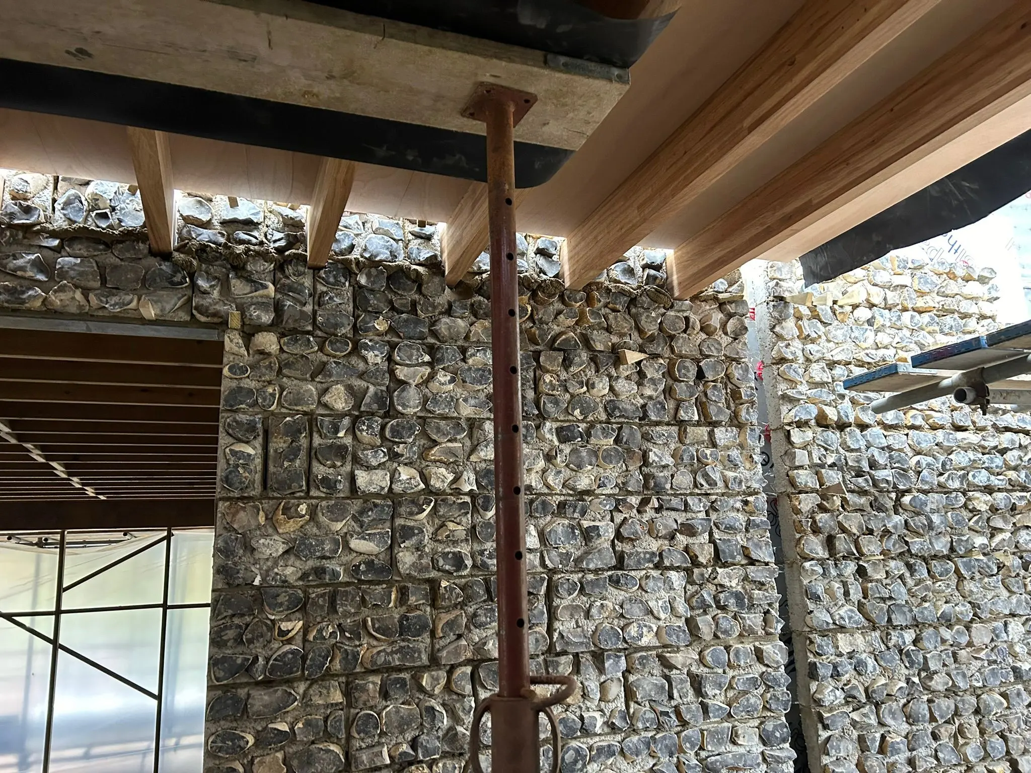 Acrow prop supporting timber formwork above a flint stone wall on a construction site