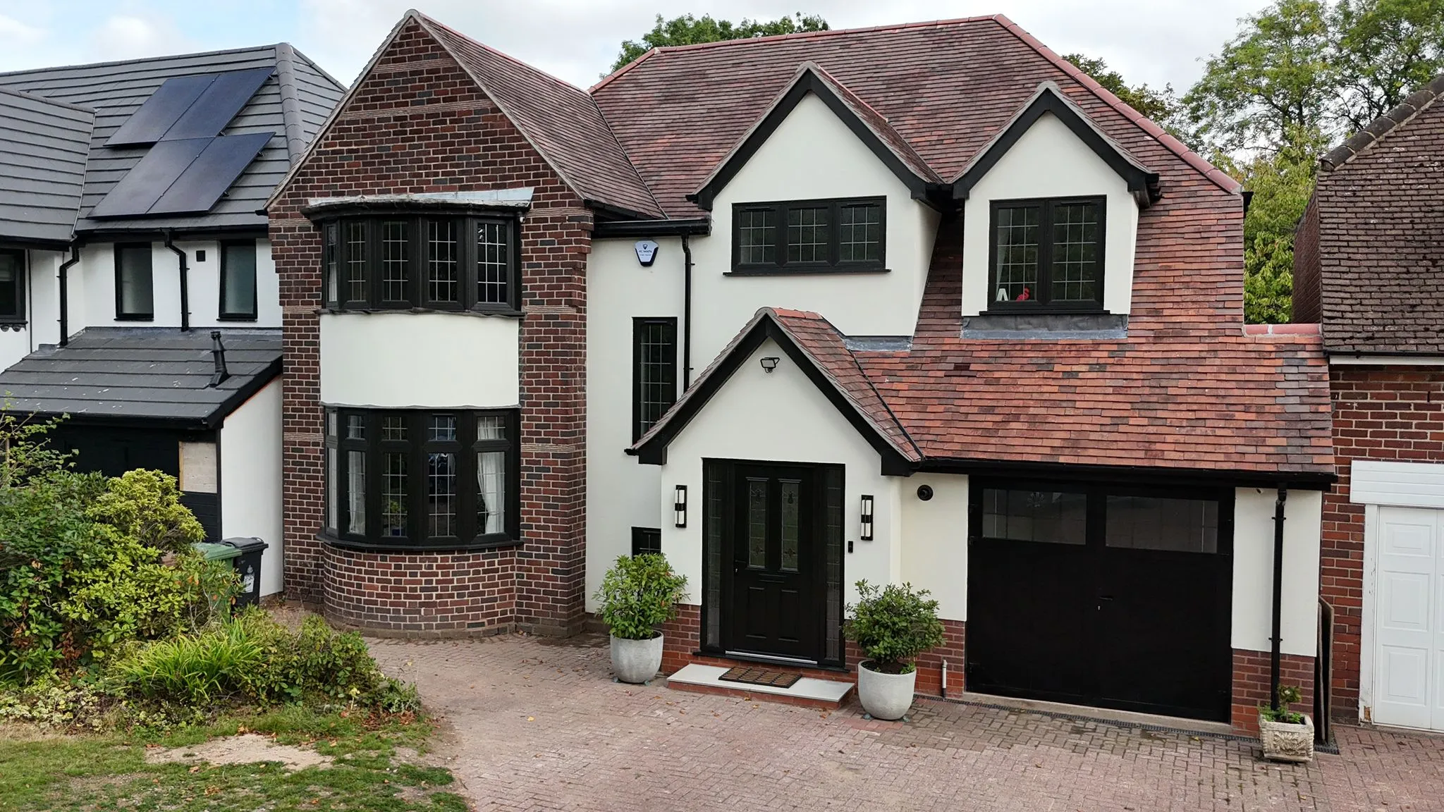 A modern detached house with white render, red brick, dark windows, and a paved driveway, showcasing high-quality building work.