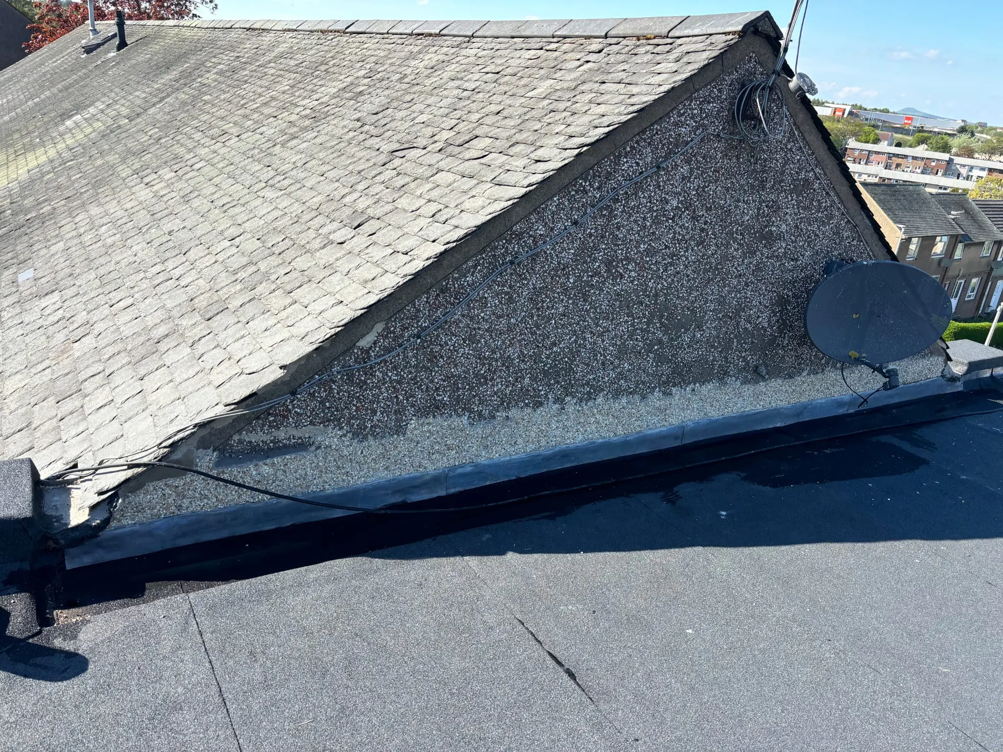 Newly installed flat roof meeting a roughcast wall and pitched slate roof with lead flashing
