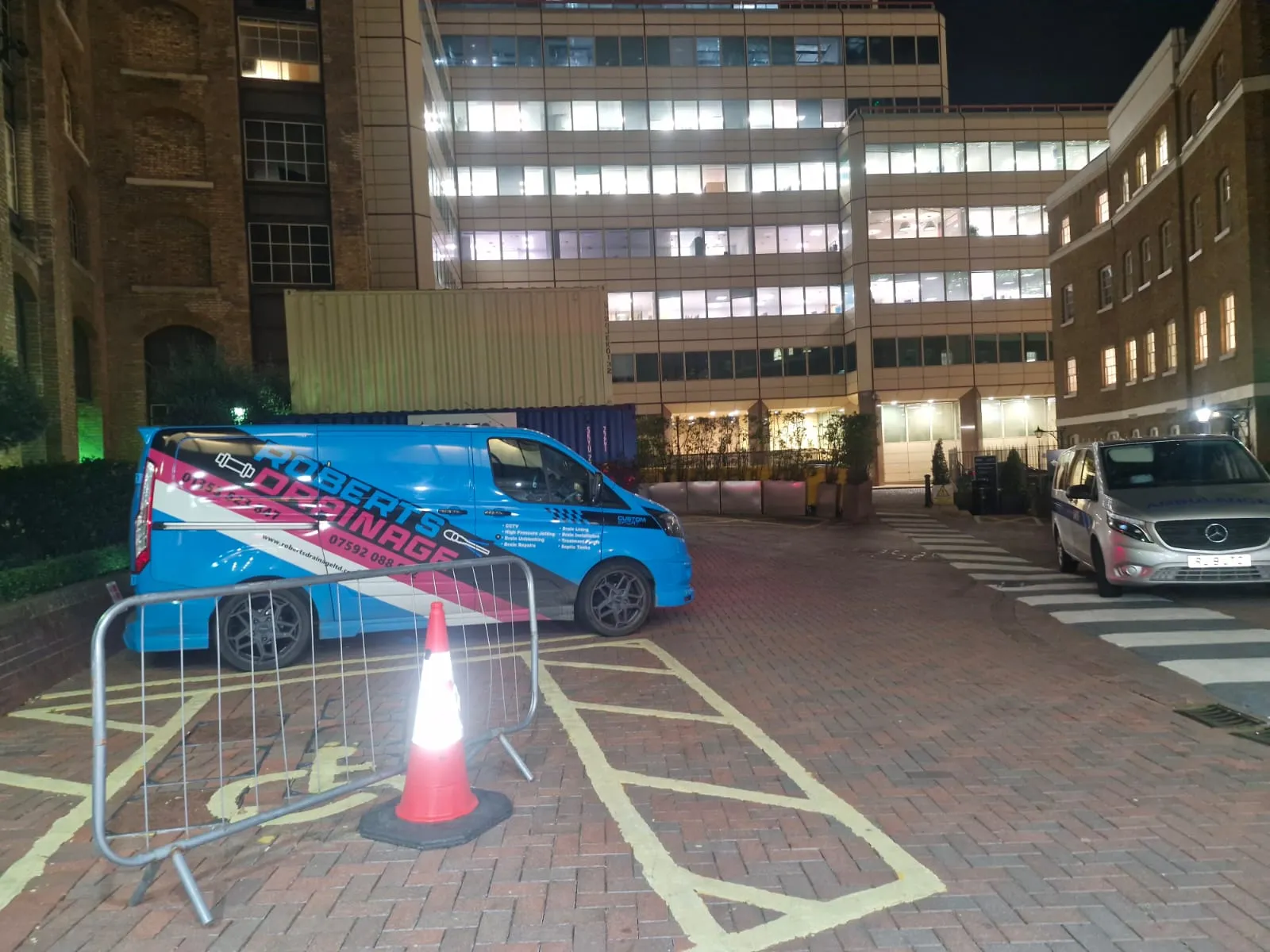Roberts Drainage Ltd service van parked outside a commercial building at night in a city setting.