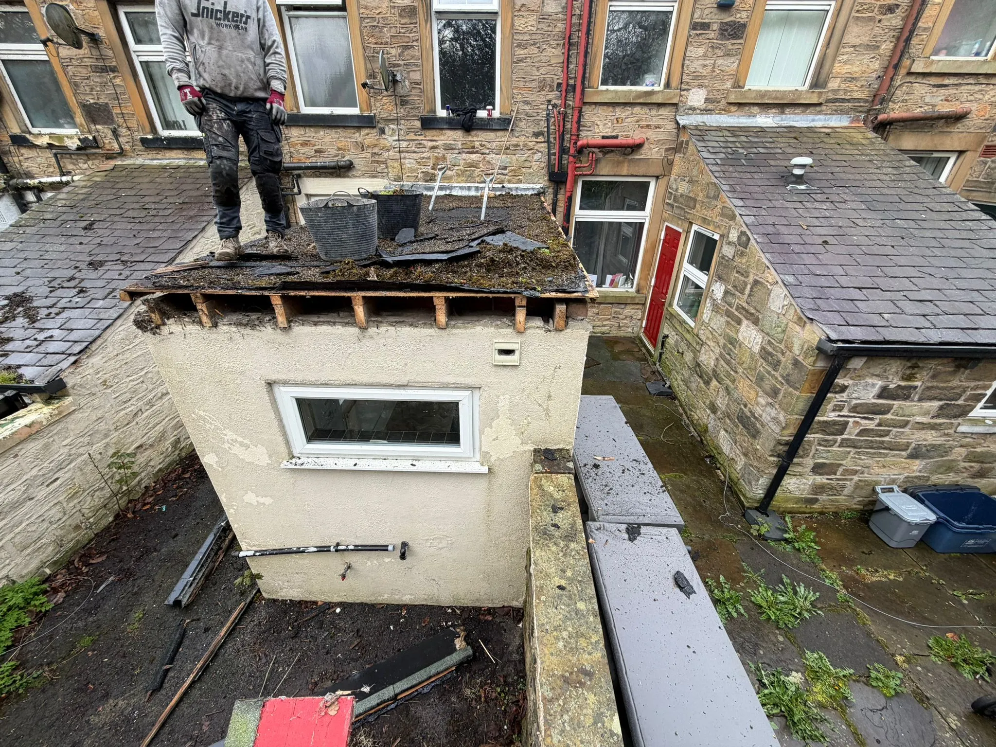 A roofer removing old felt from a flat roof during a replacement project in Blackburn.