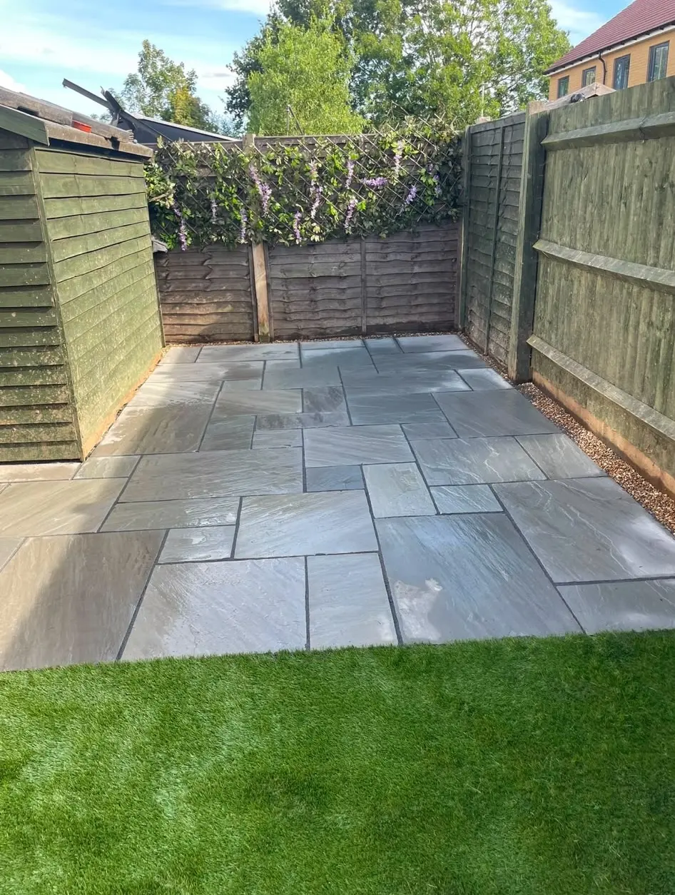 A freshly laid grey Indian sandstone patio with neat pointing and drainage borders in a Northampton garden.