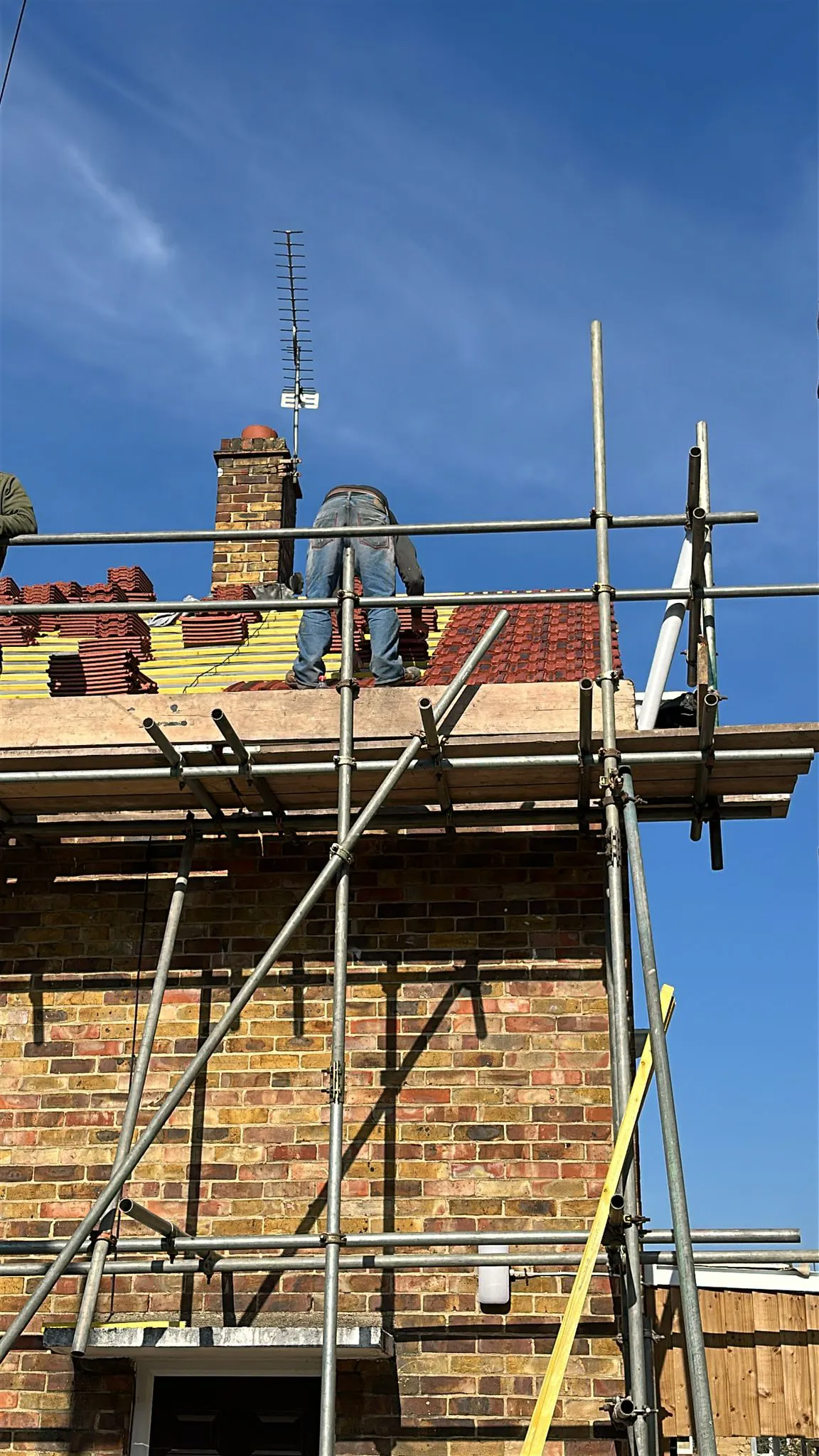 Roofer laying red roof tiles on a pitched domestic roof replacement project