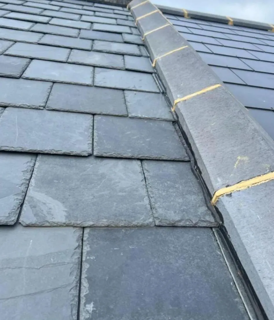 Close-up view of freshly laid natural slate tiles and mortar-bedded ridge caps on a pitched roof