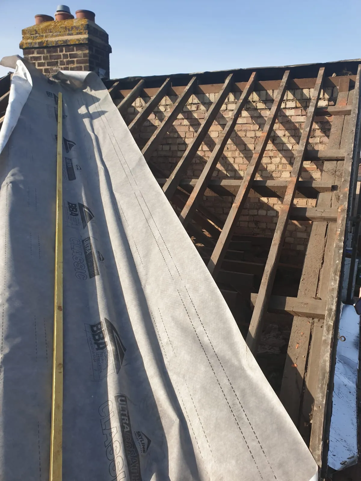 Installation of breathable roofing membrane over timber rafters during a re-roofing project.
